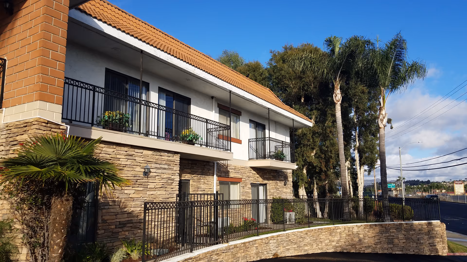 Two-story senior living building with stone facade, balconies, and palm trees outside.