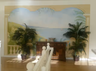 Interior hallway with an ocean mural, palm plants, and a wooden console table.