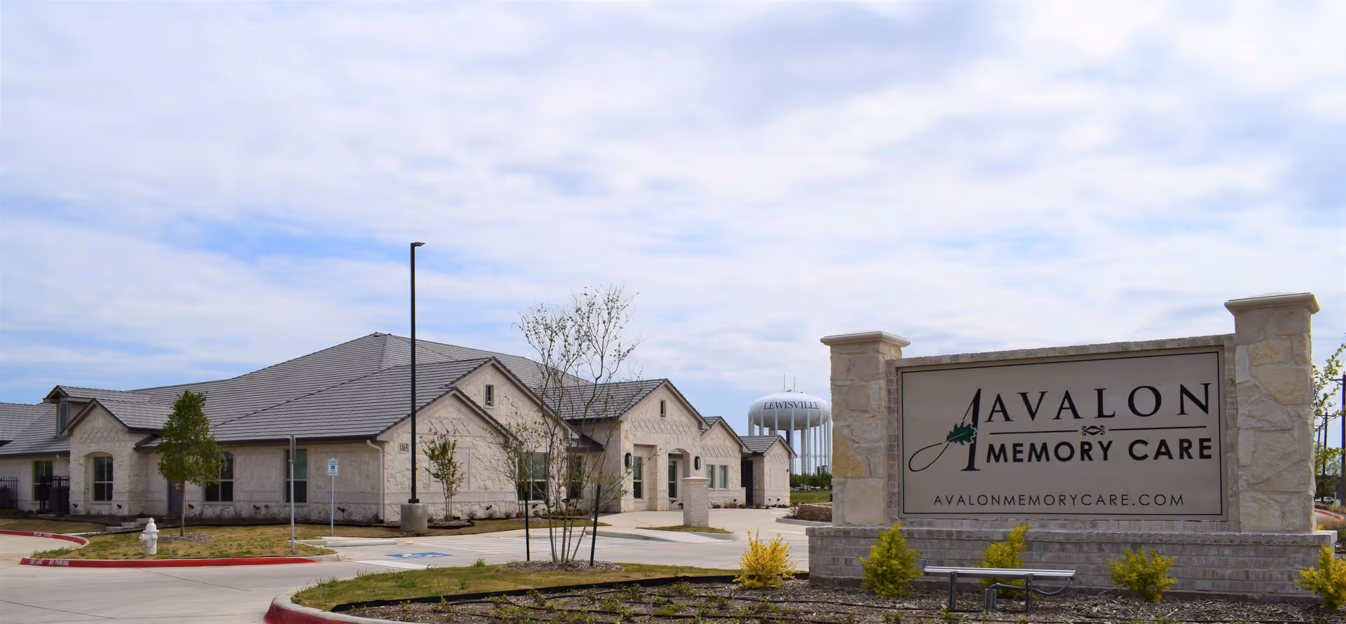 Exterior view of Avalon Memory Care facility with entrance, sign, and landscaping.