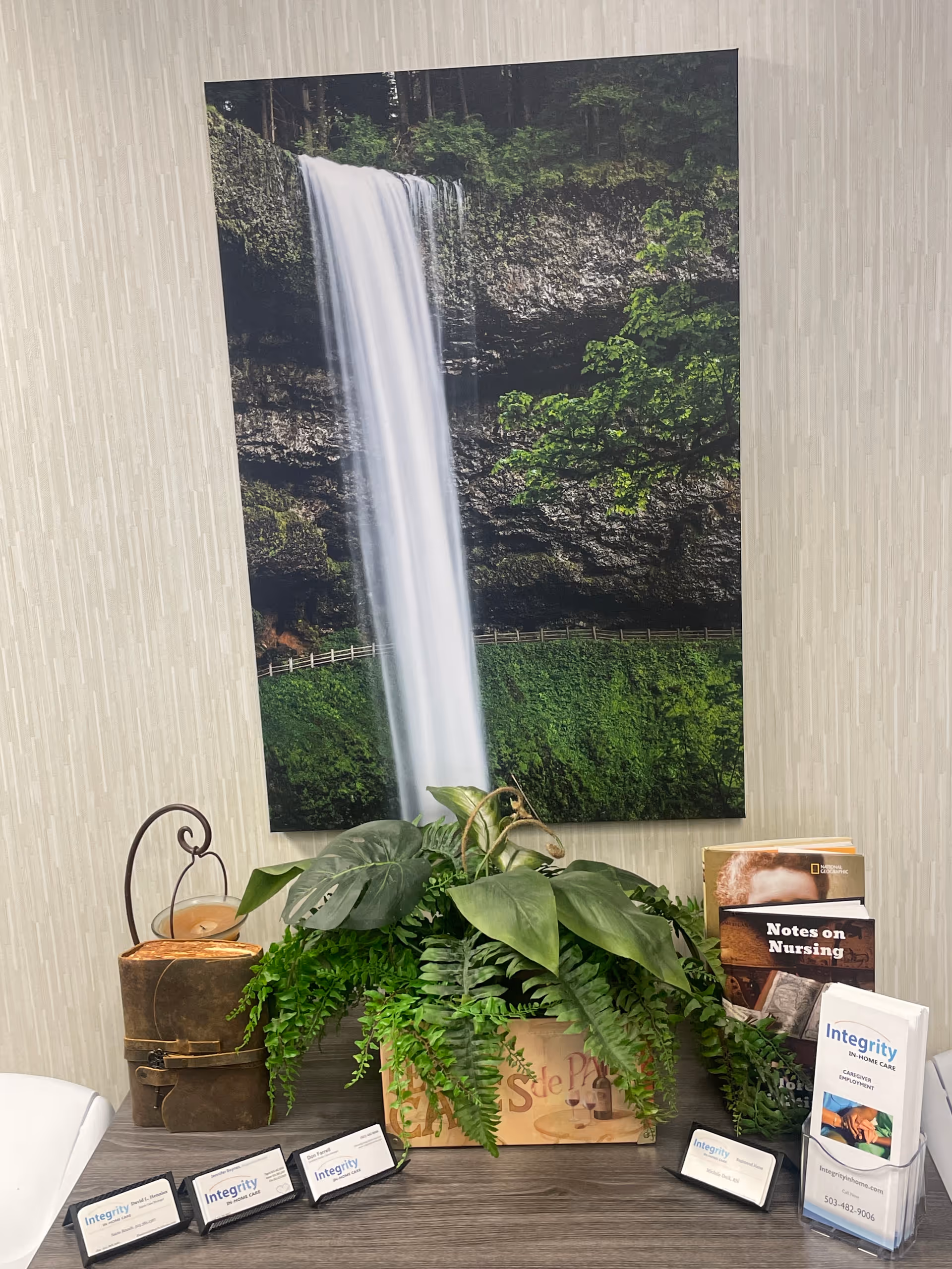 Indoor lobby with waterfall poster, lush plants, and brochure display.