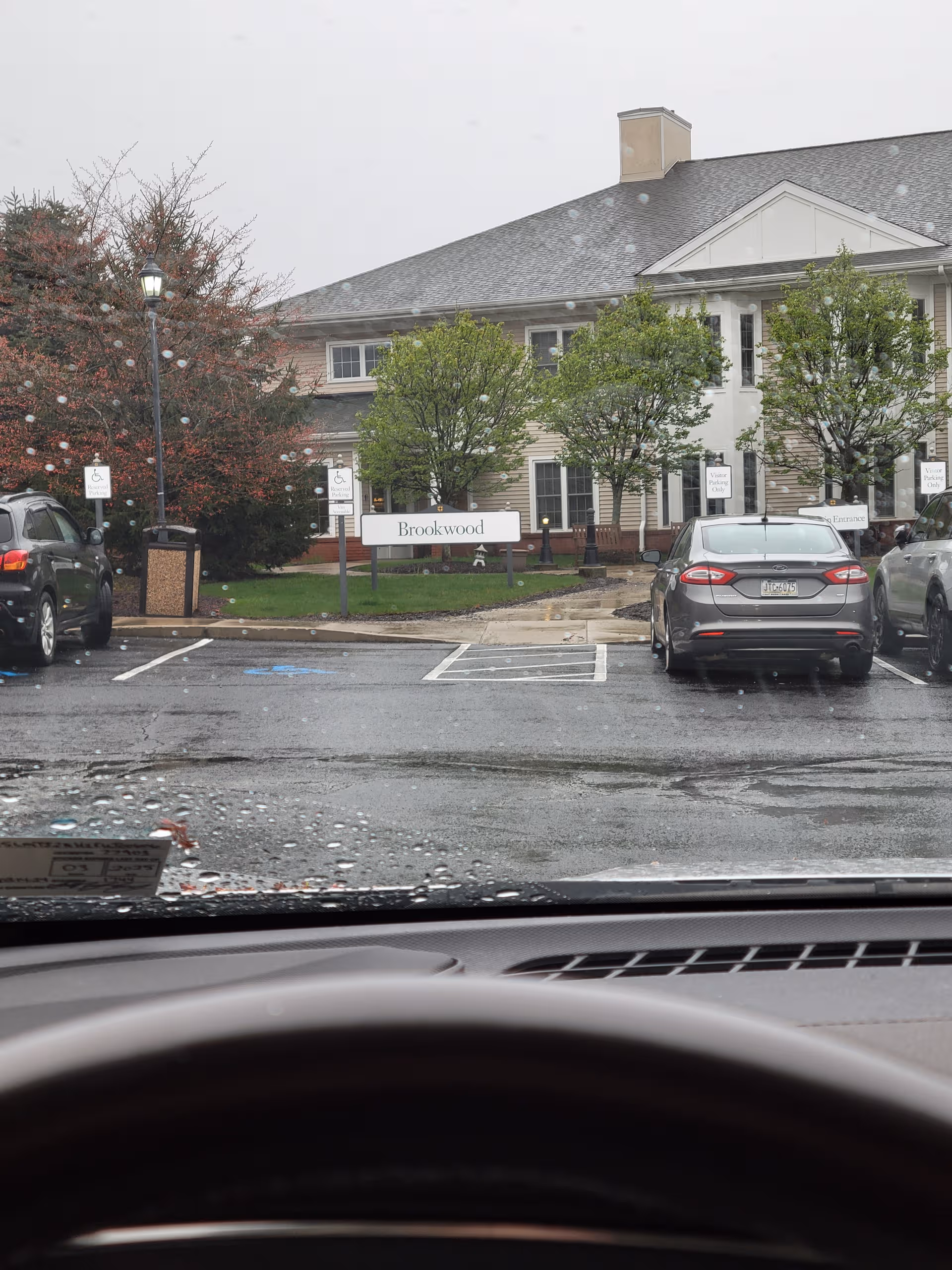 Front exterior of Brookwood retirement community with parked cars and trees.