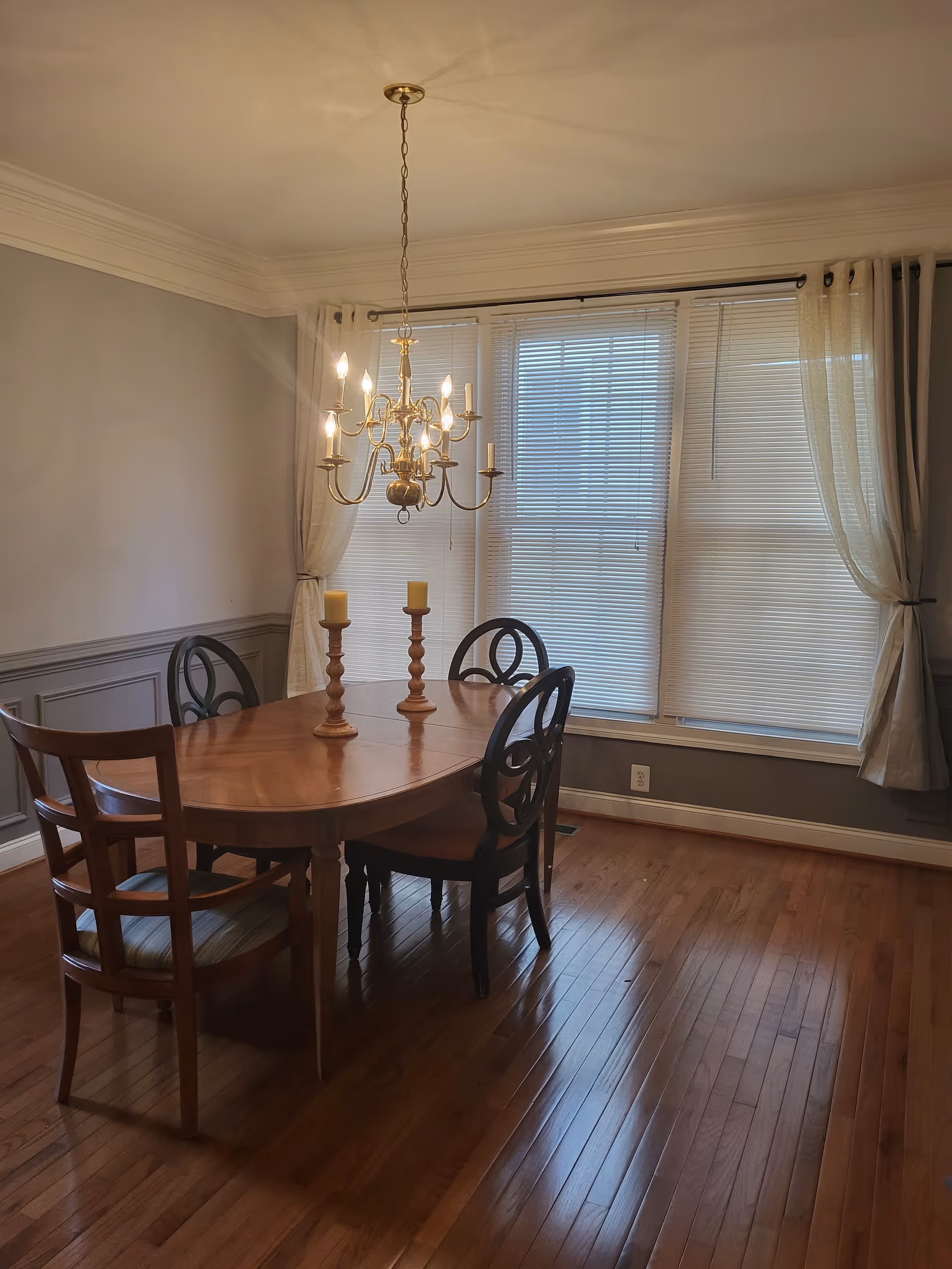 Wood dining room with a wooden table, chairs, chandelier, and large windows.
