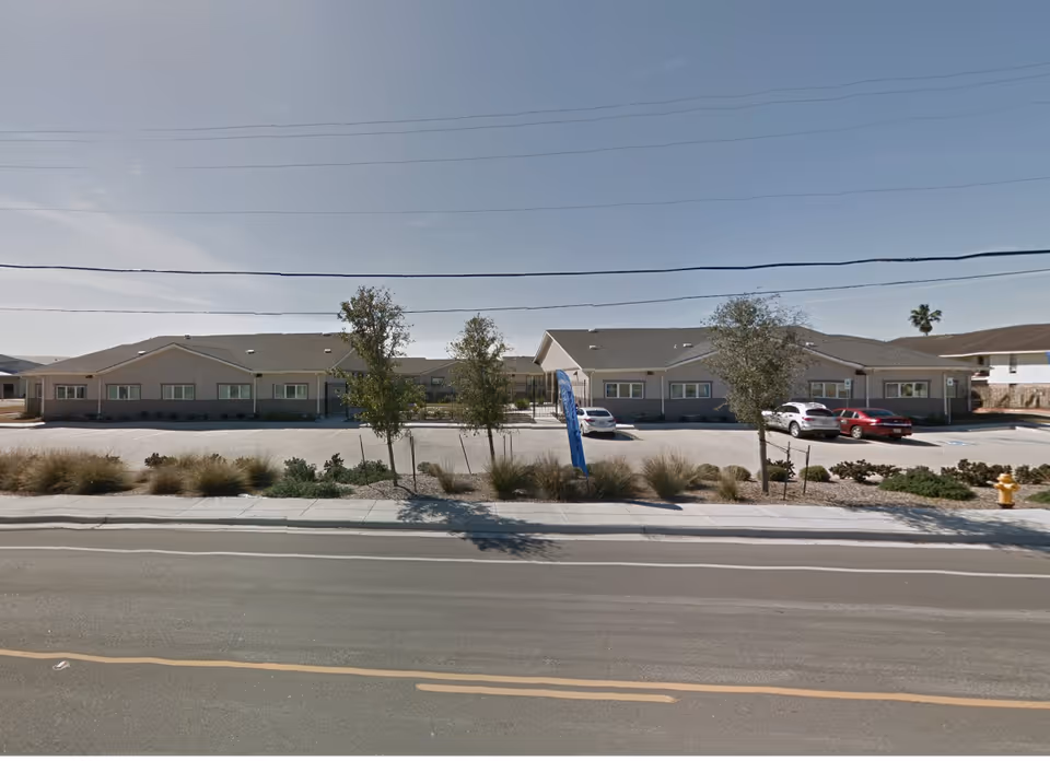 Single-story memory care facility with a long front facade and parked cars.