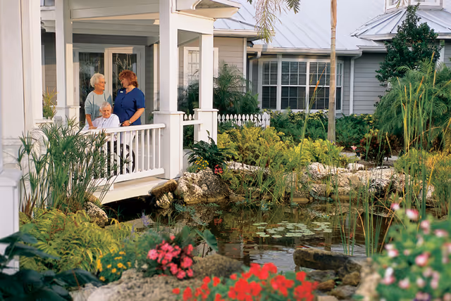 Three people on a porch by a landscaped pond in front of a hospice house