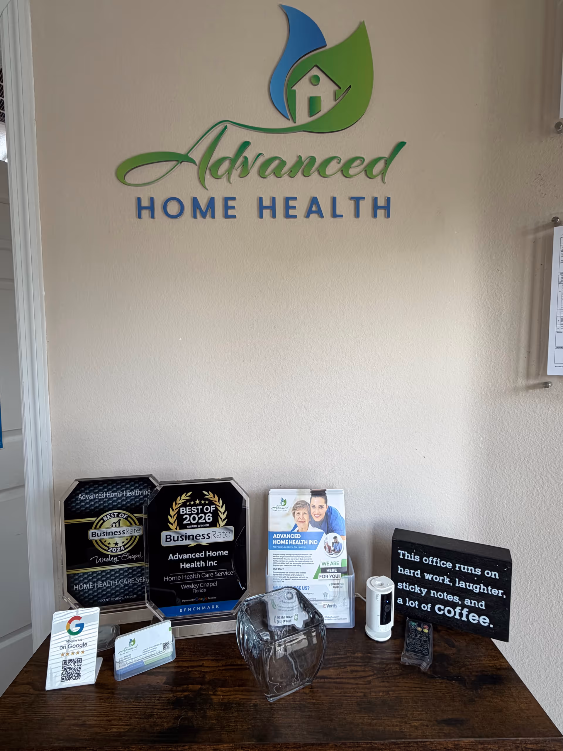 Interior wall displays Advanced Home Health logo with awards and brochures on a desk.