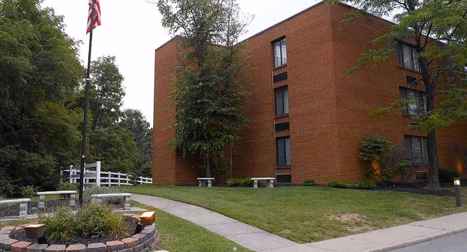 Front exterior of Celebration Villa of Highland Crossing, with lawn, trees, benches, and flagpole.