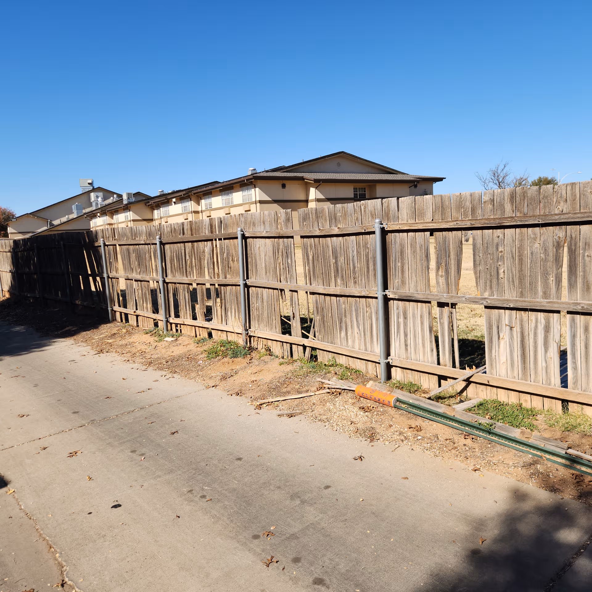 Blue sky above a tall wooden fence with a beige apartment-style building behind.