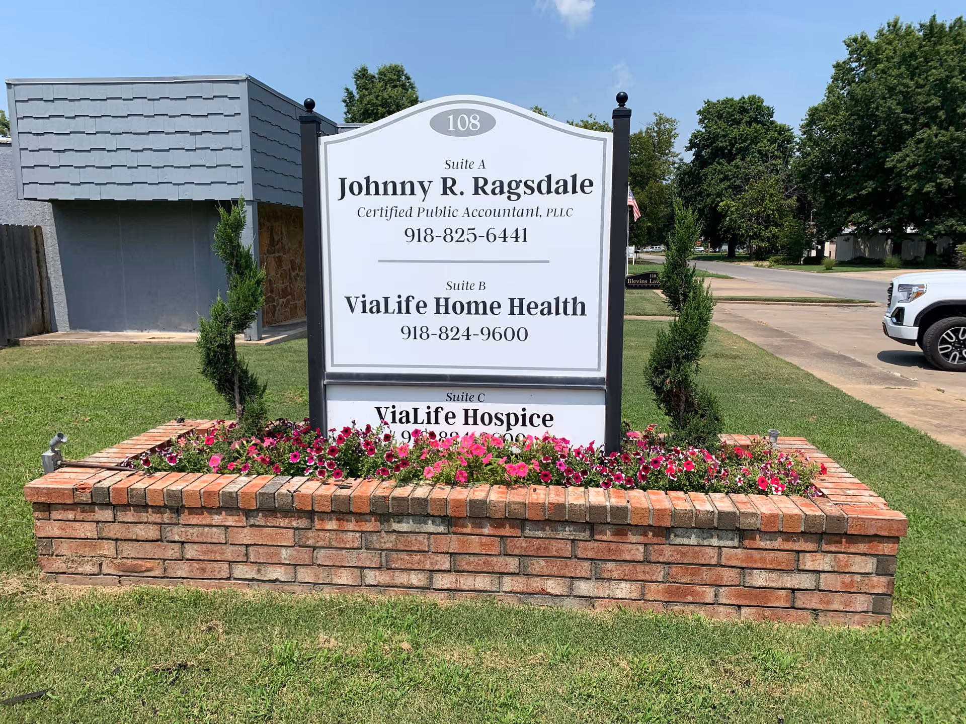 Outdoor sign for ViaLife Home Health and Hospice among flowers and brick planter.