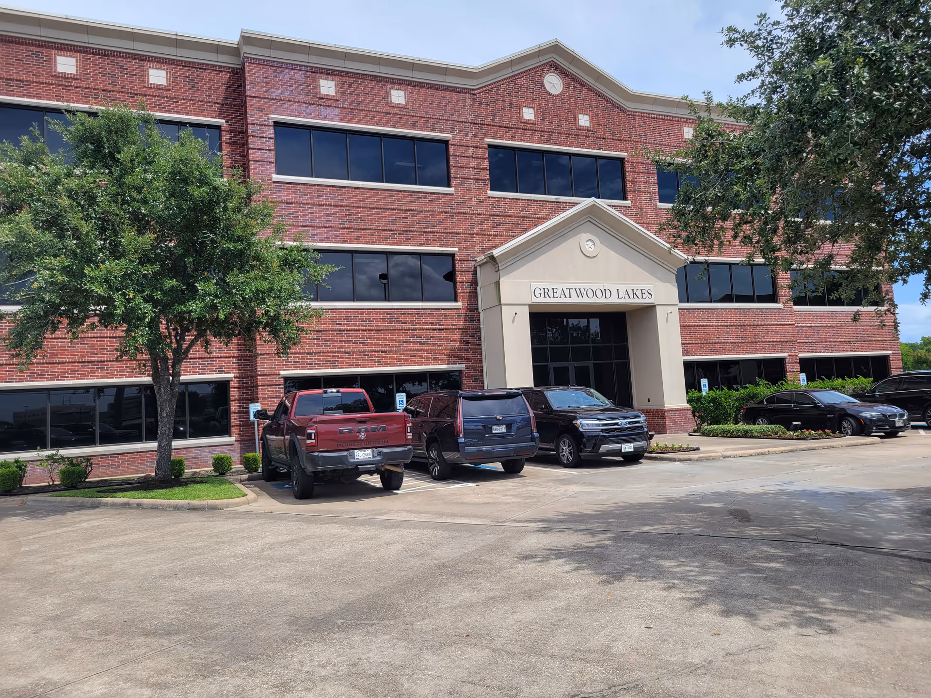 Brick senior living facility with glass entrance and parked cars in front