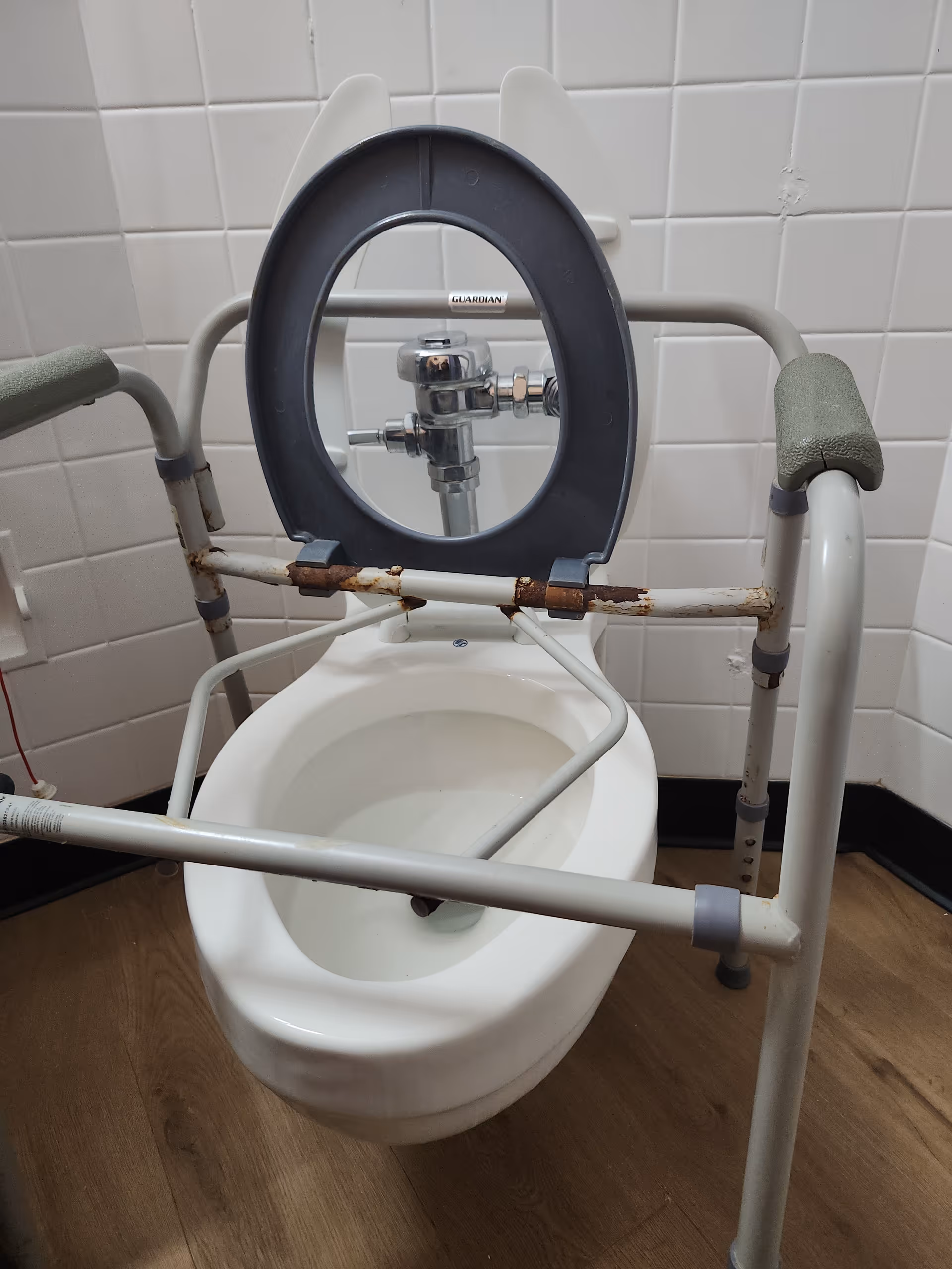 Accessible bathroom with a commode chair and support rails in a tiled room.