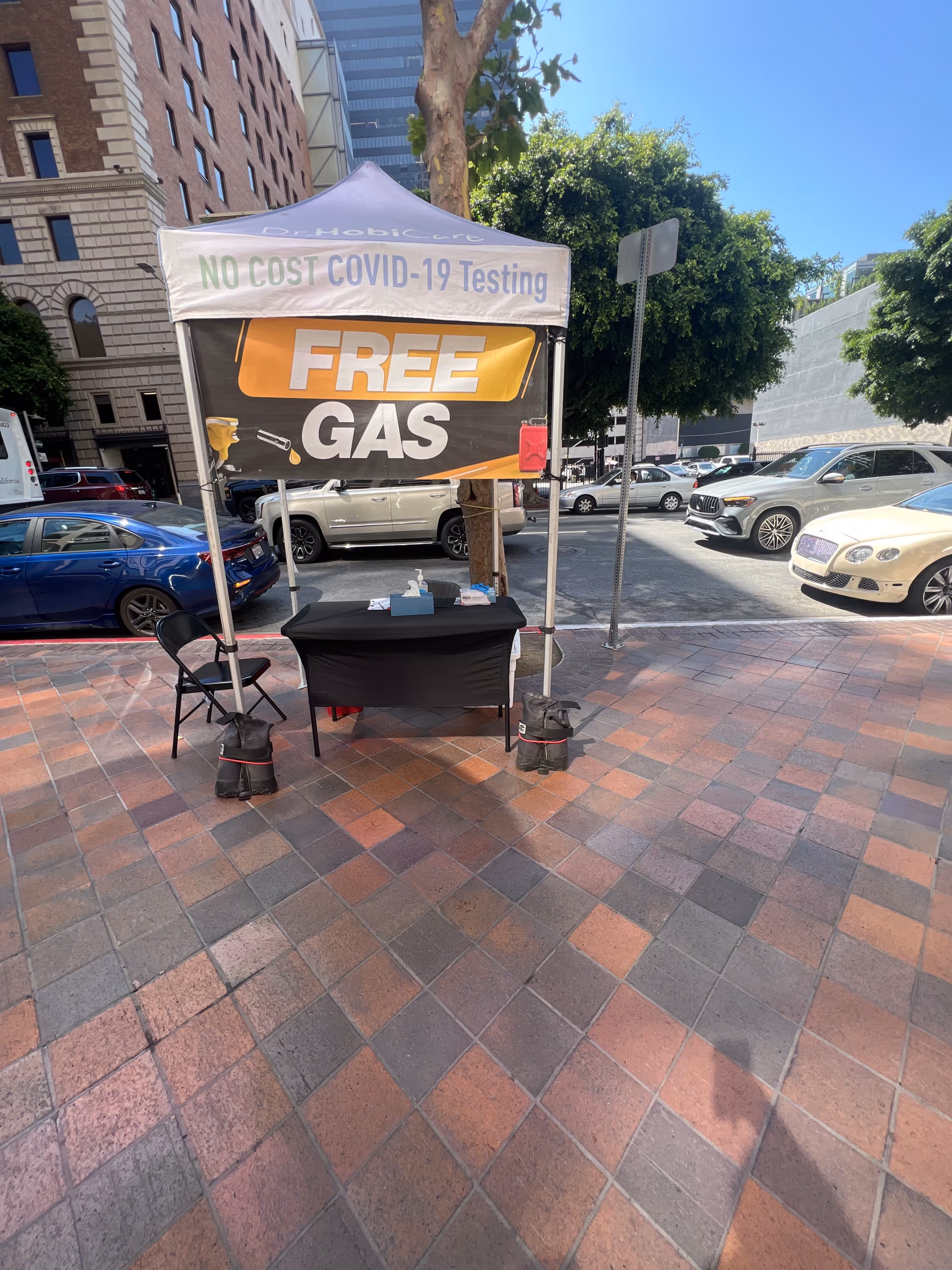Outdoor tent setup with No Cost COVID-19 Testing and Free Gas banners in plaza.