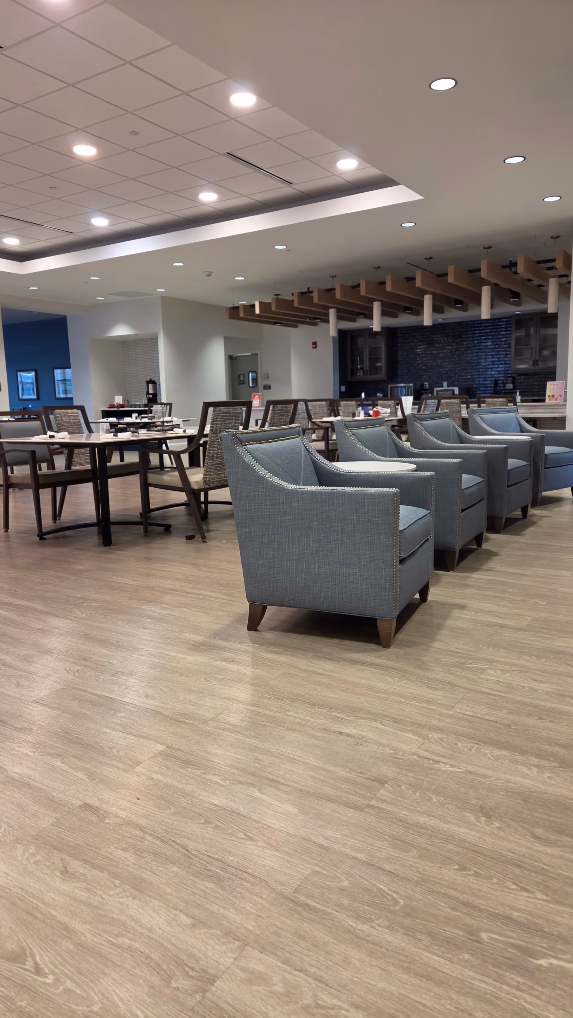 Spacious indoor lounge area with blue armchairs, dining tables, and a kitchenette.
