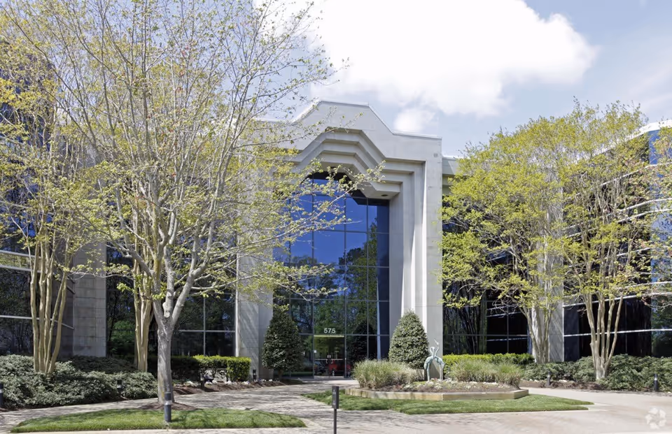 Modern building with a glass entry, landscaped trees, and a sculpture.