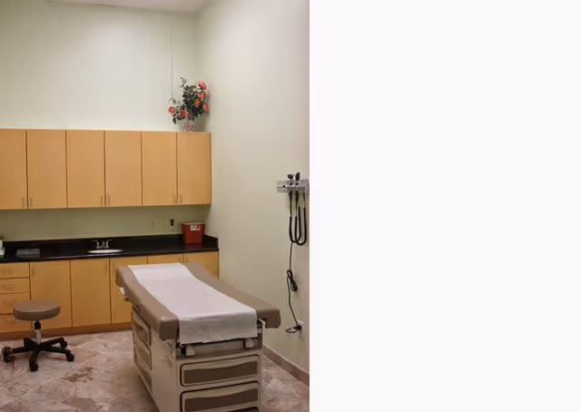 Exam room with padded treatment table, cabinets, sink, and medical equipment.