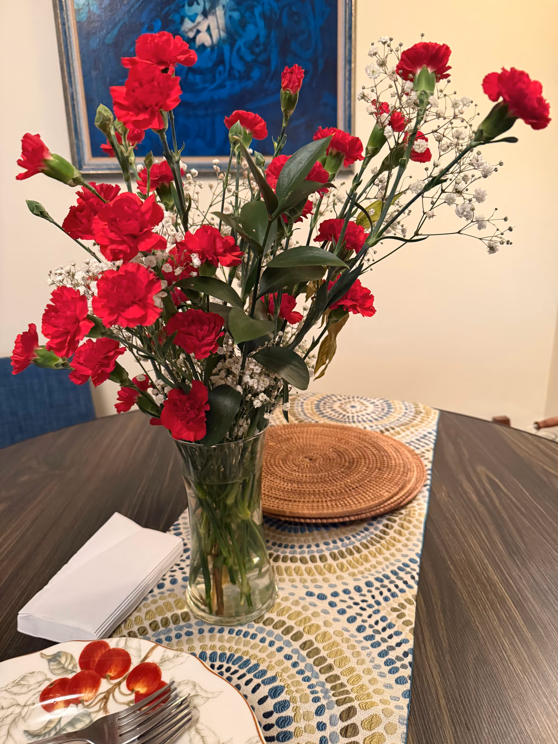 Vase of red carnations with baby's breath on a patterned dining table.