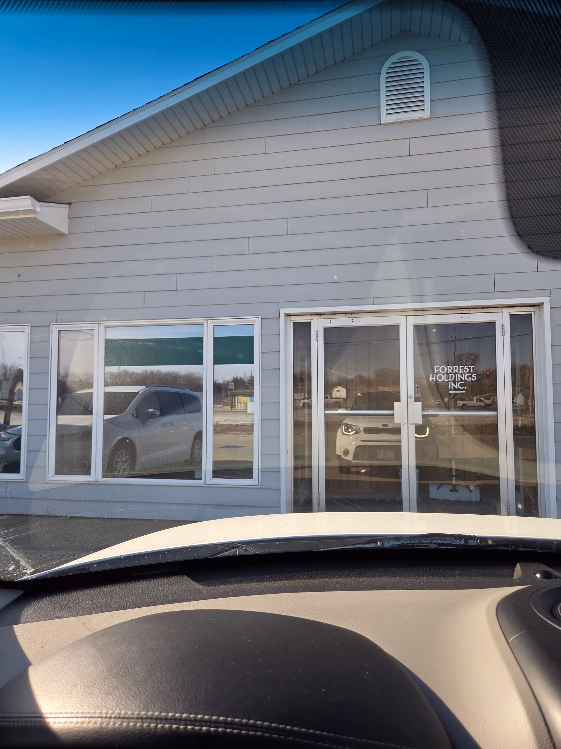 Front exterior of a light-gray building with glass entrance doors and a car parked outside.