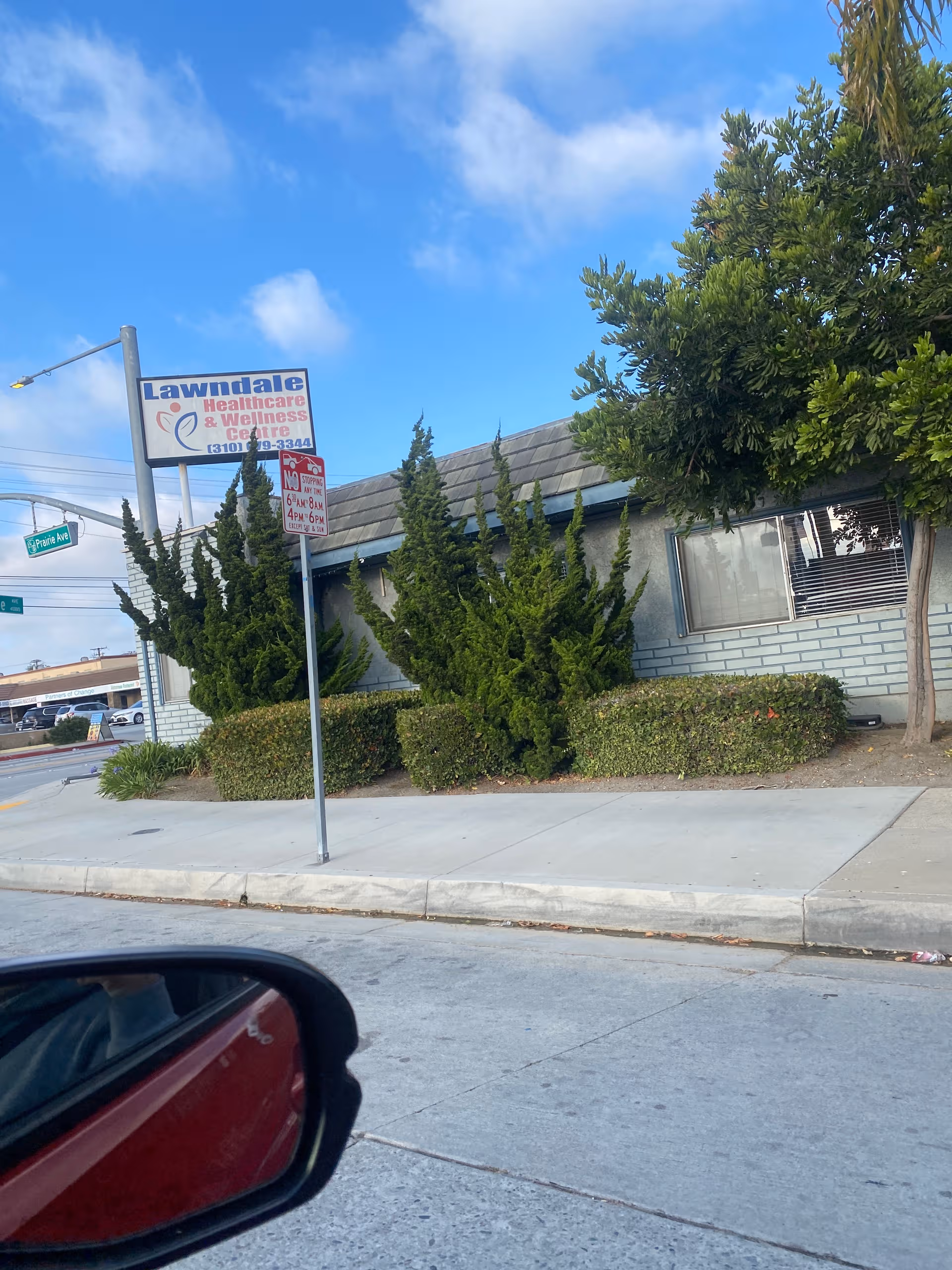 Street view of a low-rise healthcare facility with shrubs and a sidewalk.