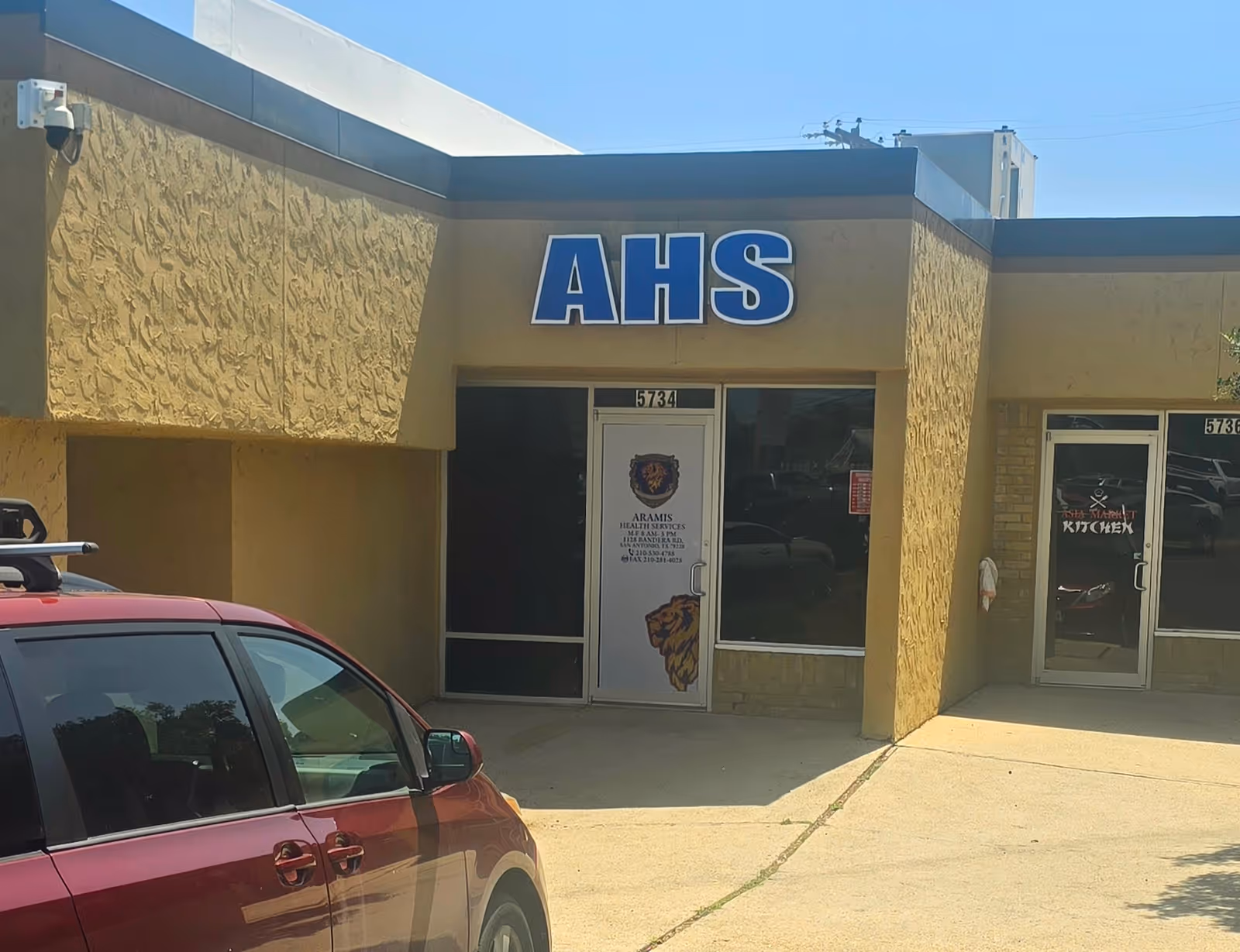 Exterior view of Aramis Health Services building with large AHS sign and a parked red car.