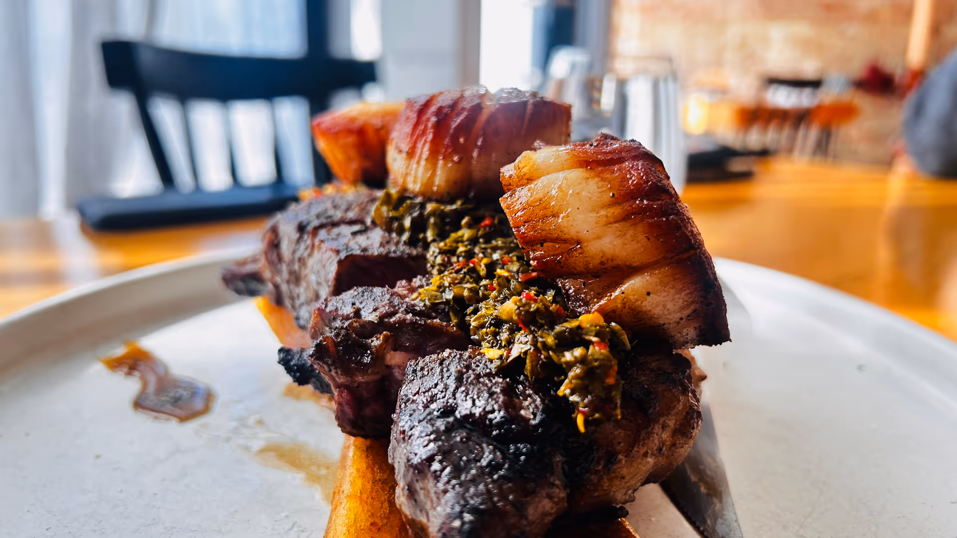 Close-up of a plated roasted meat dish with herb sauce on a dining table.