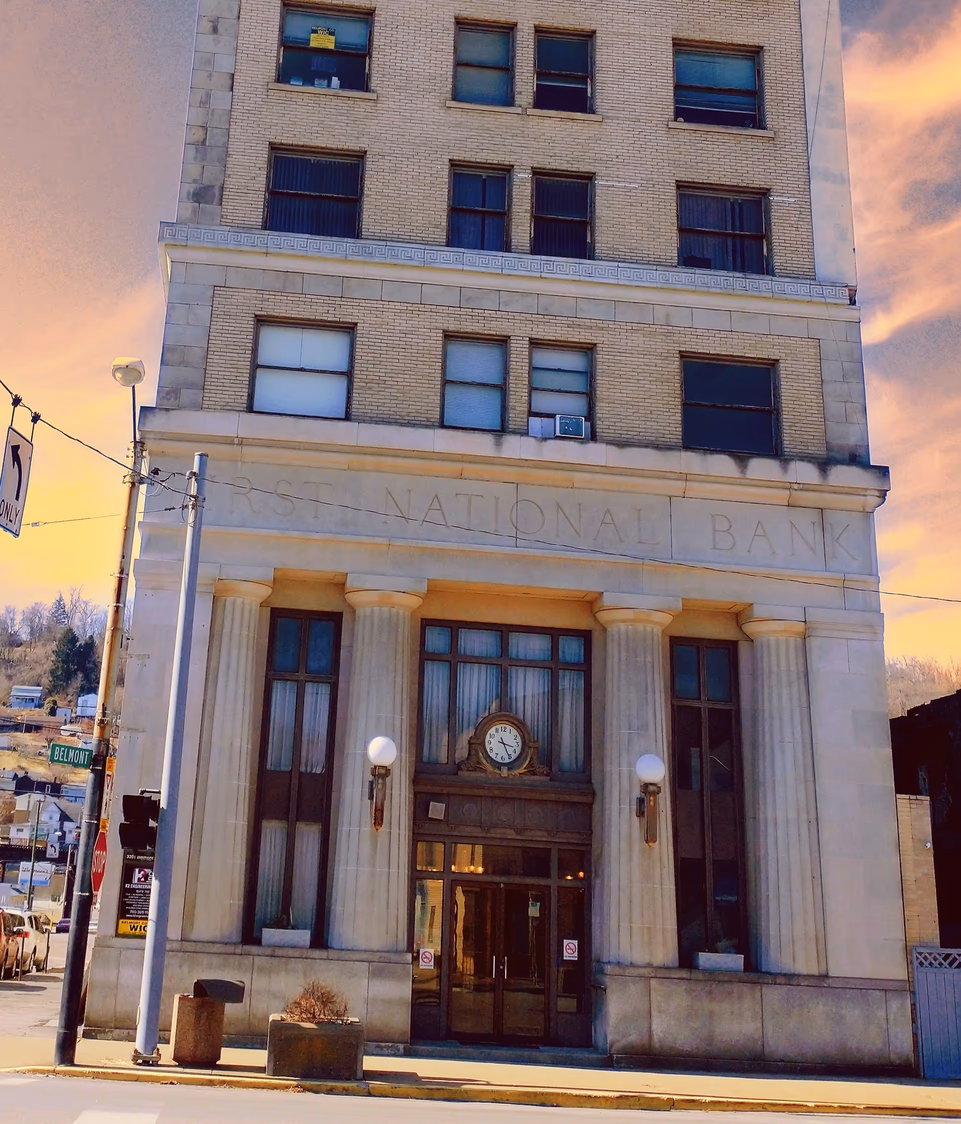 A tall brick bank building with columns, a clock, and glass doors at the entrance.