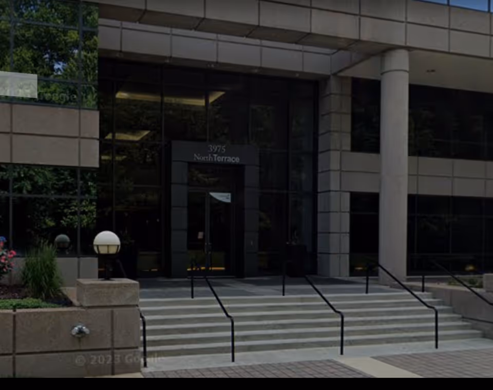 Modern office building entrance with glass walls, stairs, and ramp.