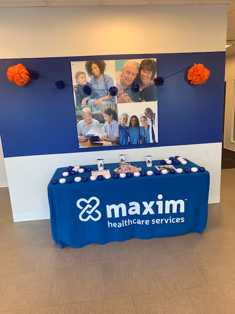 Promotional Maxim Healthcare table with photos on a blue wall in lobby.