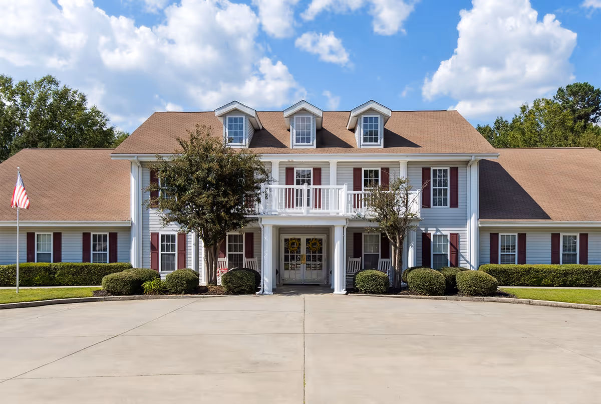 Front view of a two-story white building with red shutters, porch, and driveway.