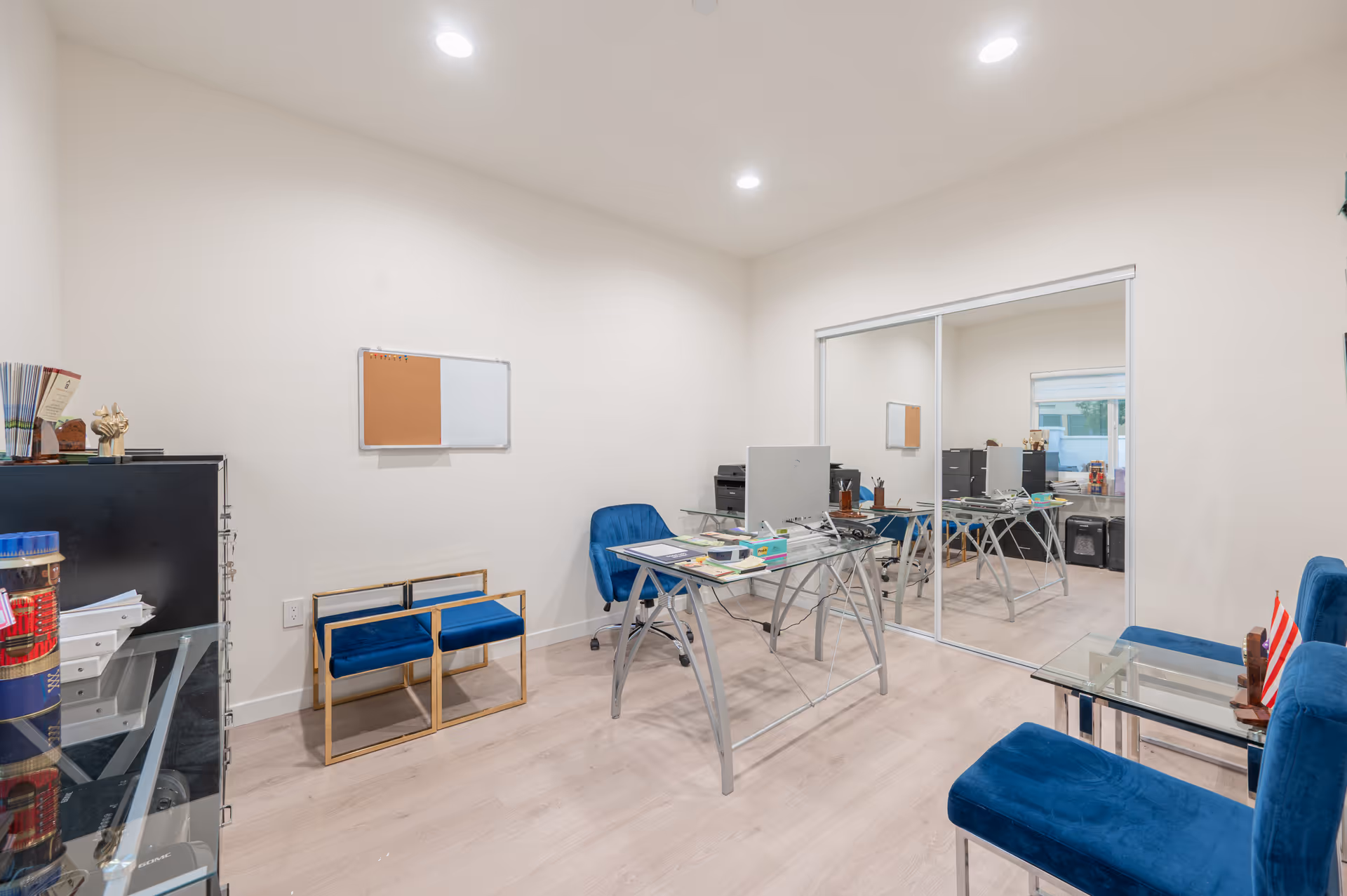 Office-like administrative workspace with glass partition, desks, monitors, and blue seating.