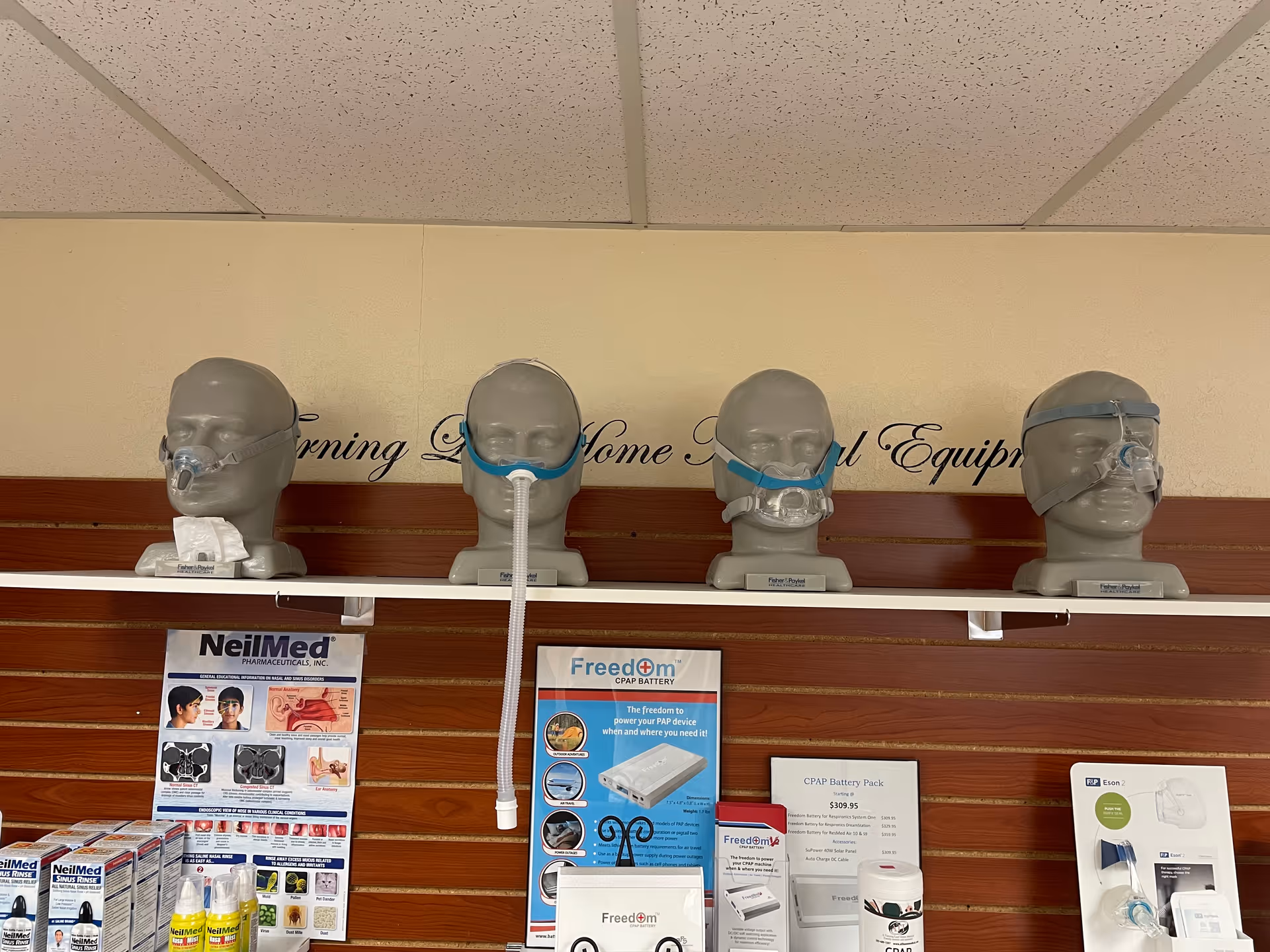 Row of mannequin heads wearing CPAP masks on a wall display in a medical equipment shop.