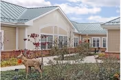 Exterior view of a light-colored senior living facility with a landscaped path and a dog