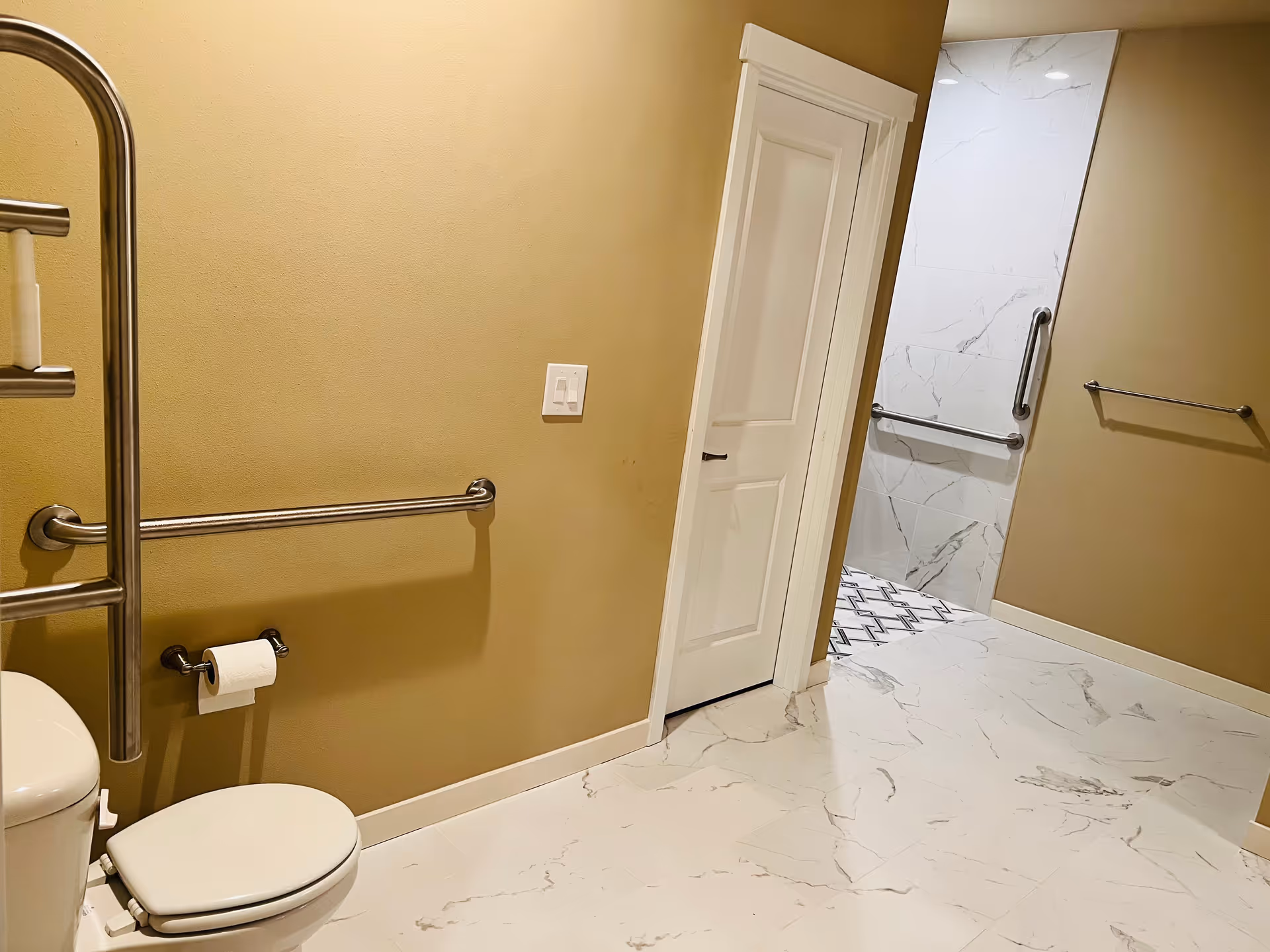 ADA bathroom in beige tones with grab bars, a toilet, and marble floor.