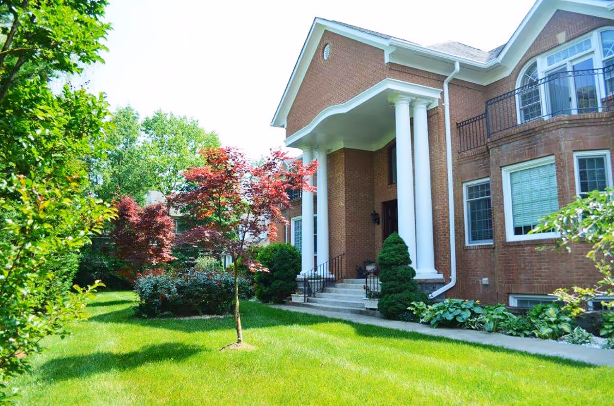 Exterior view of a brick assisted-living building with white columns and landscaped lawn.