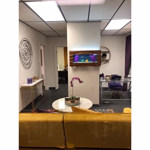 Interior living area with a yellow couch, round white table, orchid, and wall-mounted aquarium.