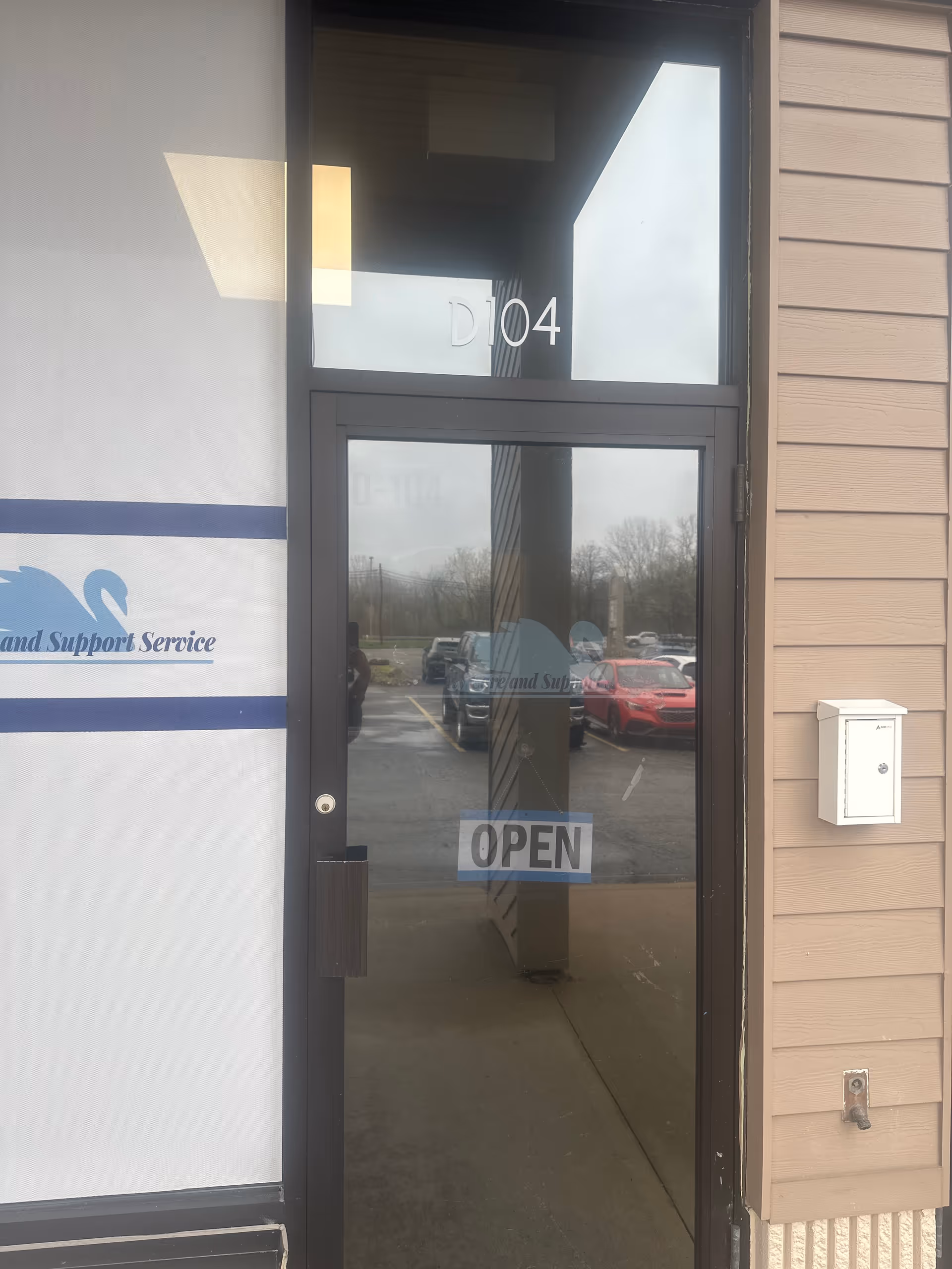Glass entrance to Serenity Care and Support Service, D104, OPEN sign, parking lot outside.