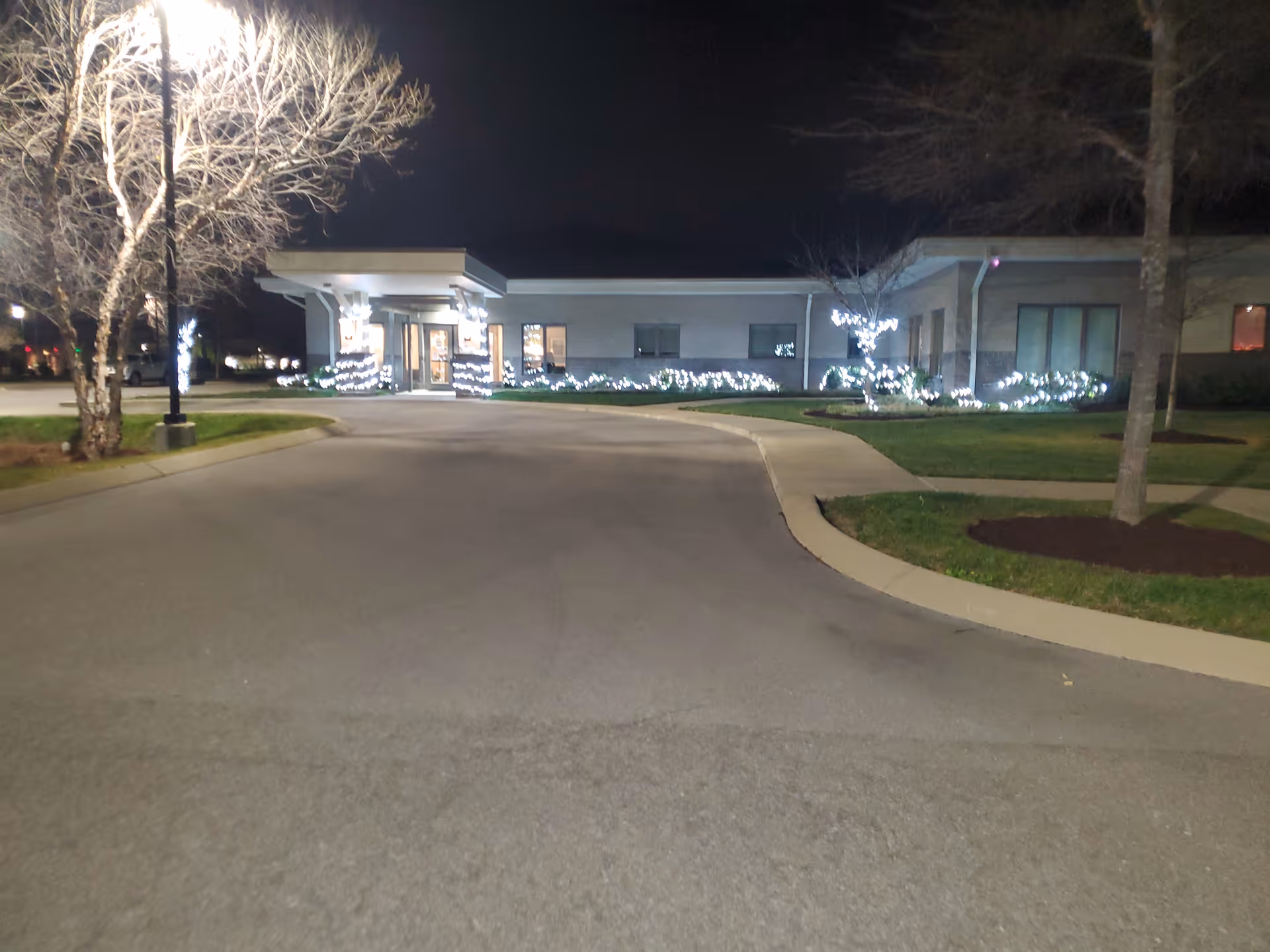Night view of the Alive Hospice front building decorated with white holiday lights along the walkway.