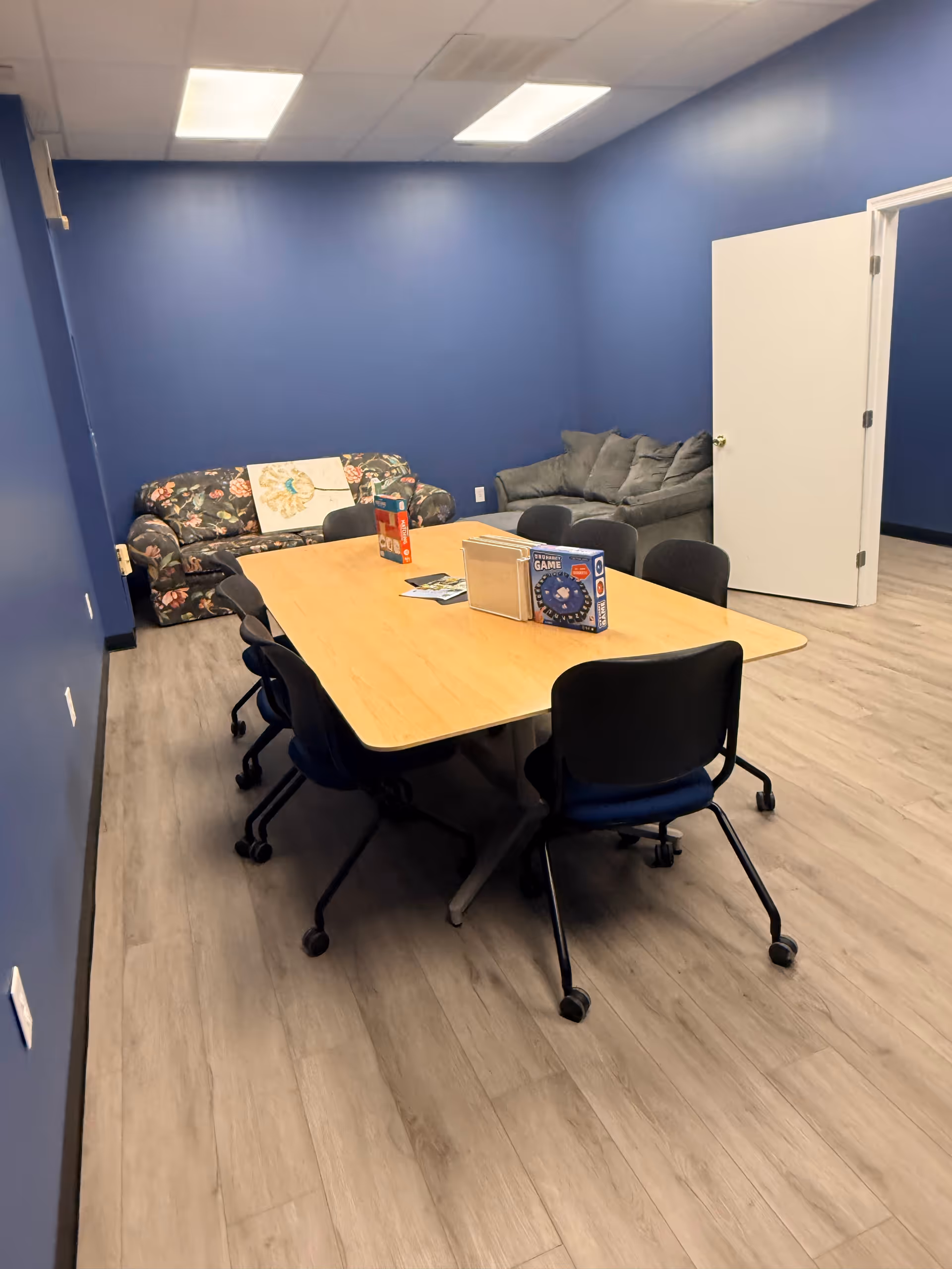 Blue-walled interior room with a long wooden table, chairs, and a couch area in back.
