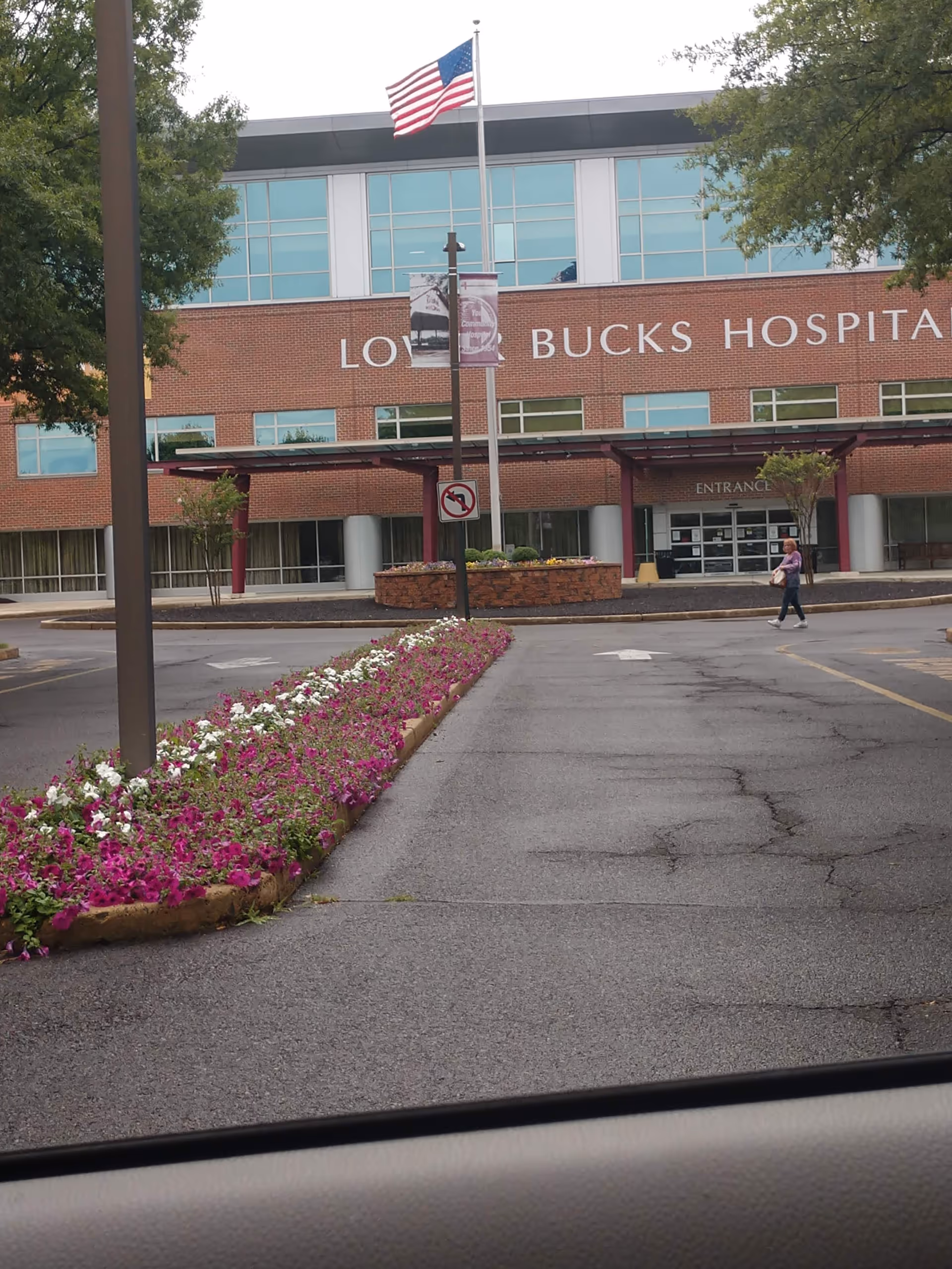 Exterior view of Lower Bucks Hospital showing brick facade, flower bed, flagpole, and entrance