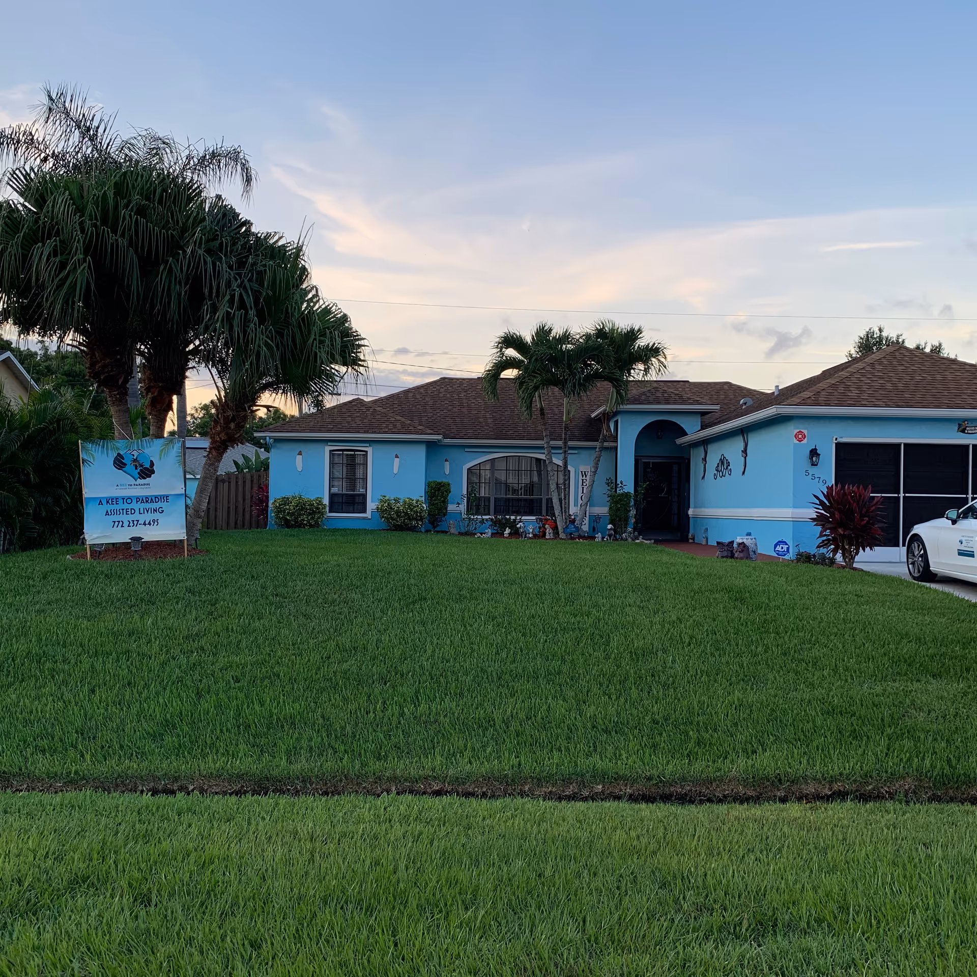 Blue single-story assisted living facility with palm trees and a grassy front yard.
