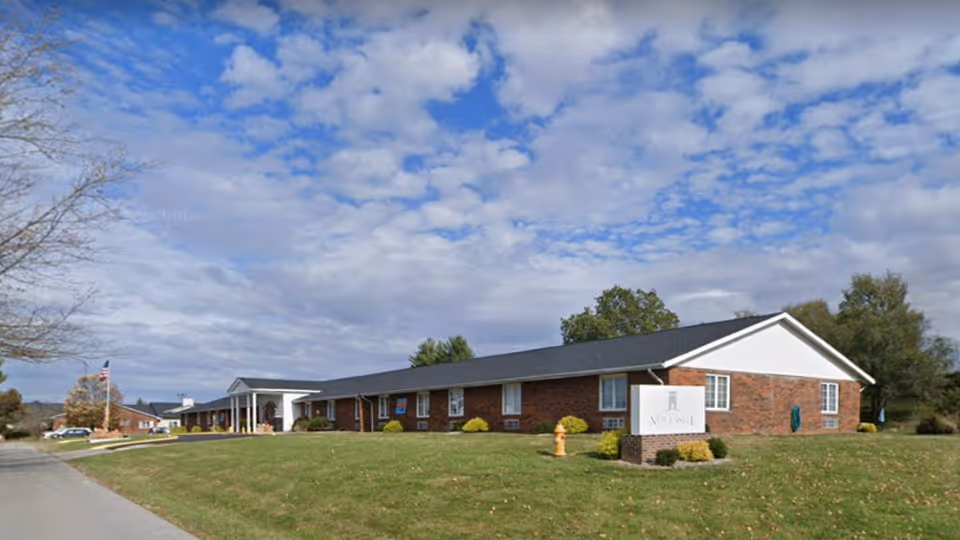 A single-story brick nursing facility with a white front entrance and a manicured lawn.