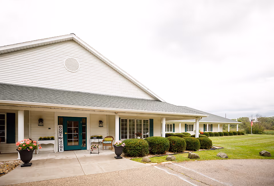 White, single-story senior living building with a covered front porch and neatly trimmed landscaping.