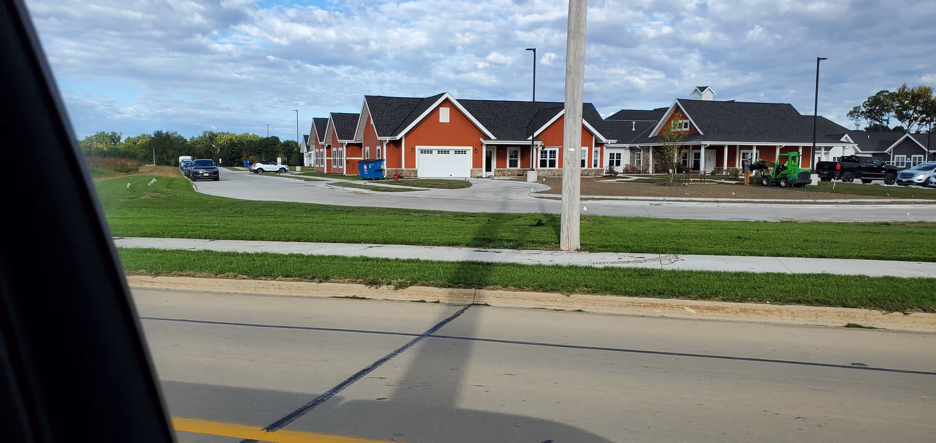 Row of red-orange townhome-style buildings with garages along a grassy median.