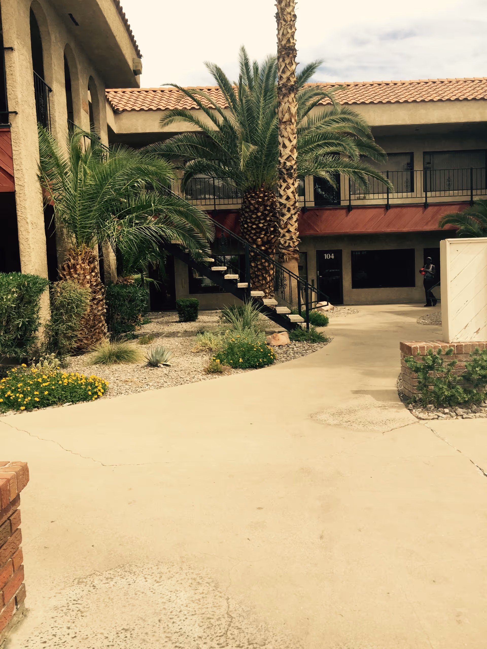Outdoor courtyard view of a two-story building with palm trees and desert landscaping.