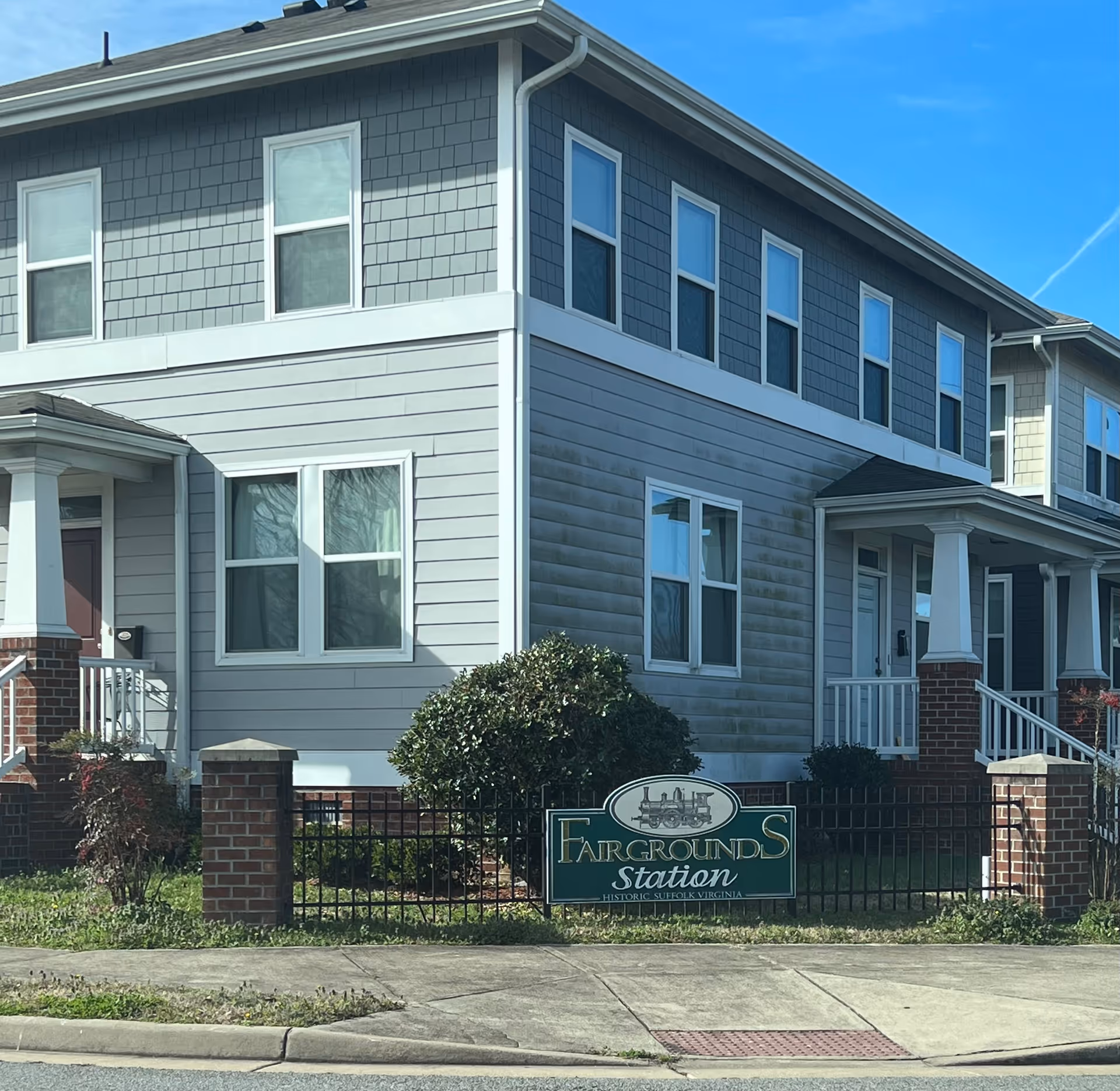 Two-story gray senior living building with a small front porch and a green sign.