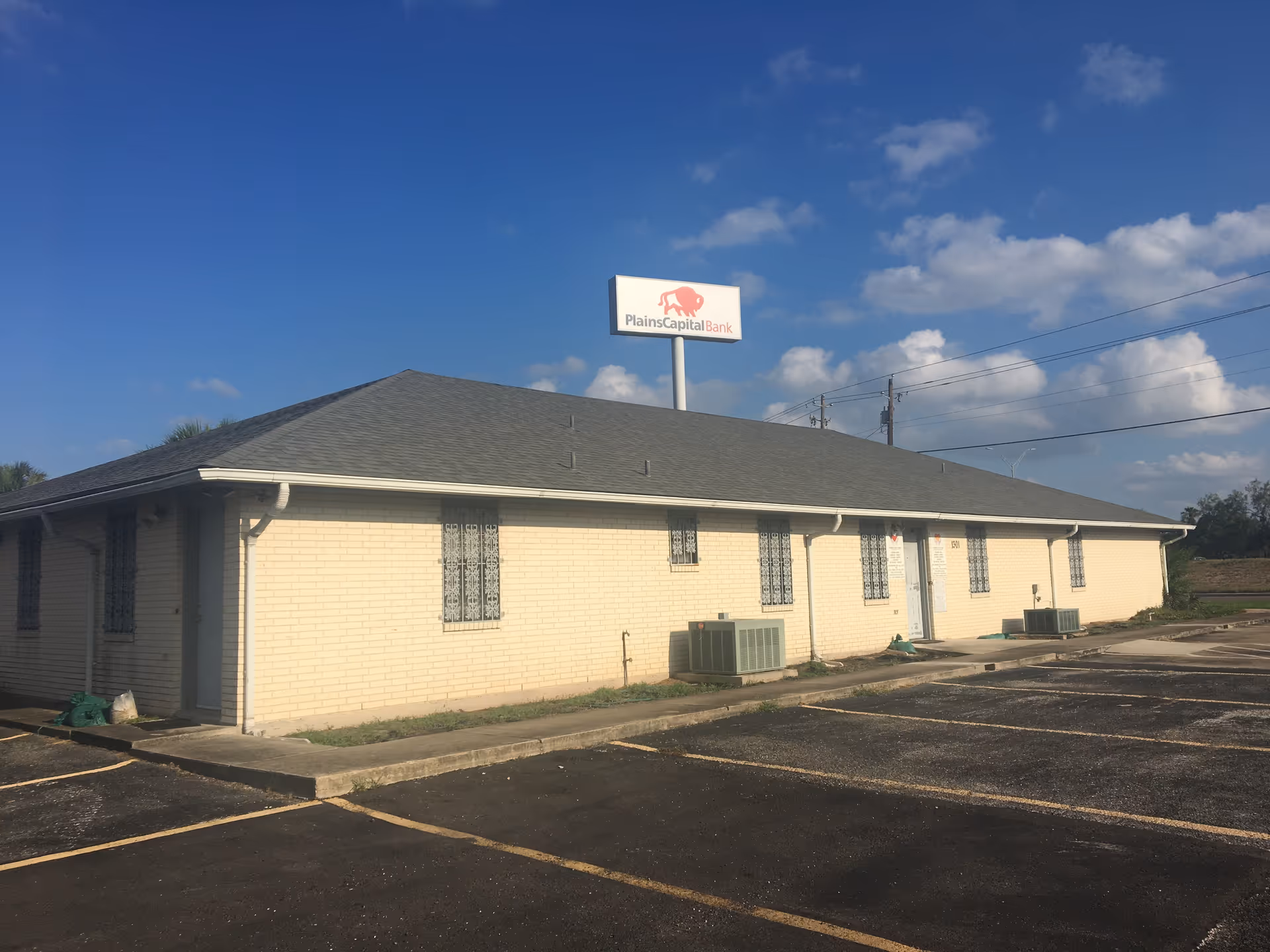 Single-story beige brick building with a bank sign and empty parking lot under blue sky.