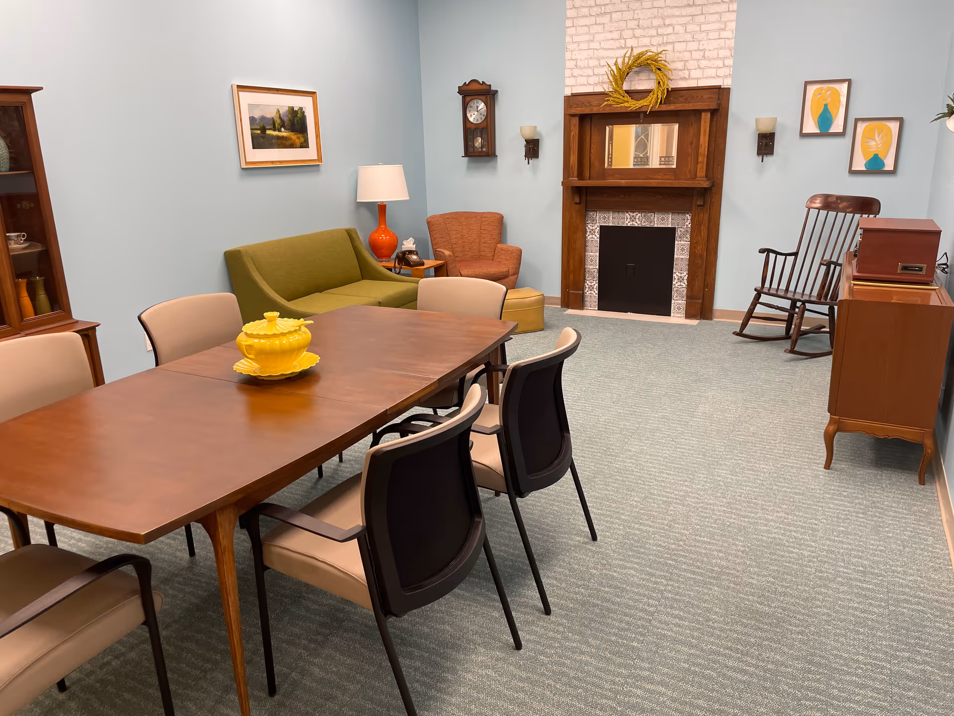 Interior common area with a wooden dining table, chairs, sofa, armchair, and fireplace.