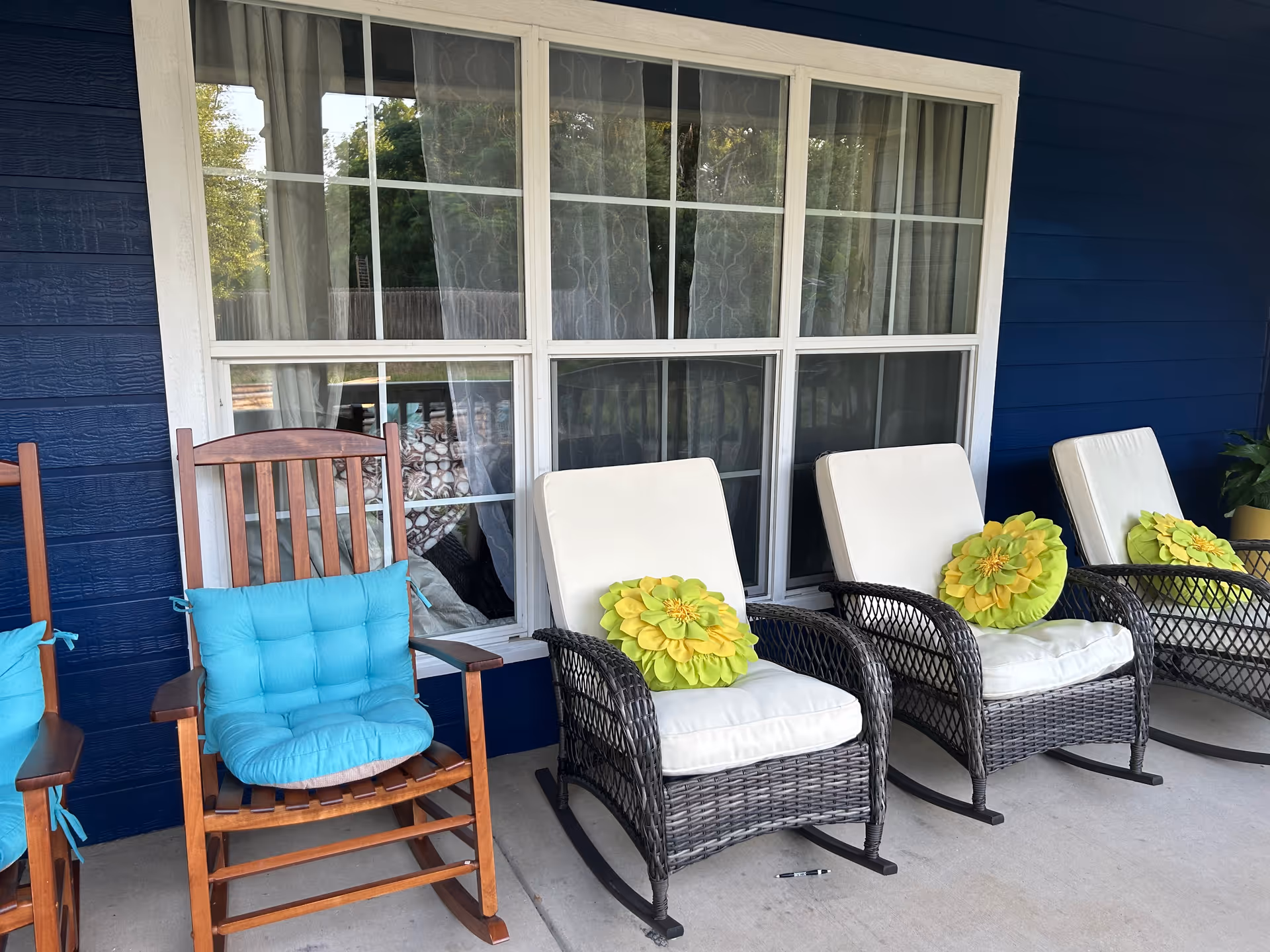 Outdoor porch with wicker chairs, a wooden rocking chair, white cushions, and flower pillows.