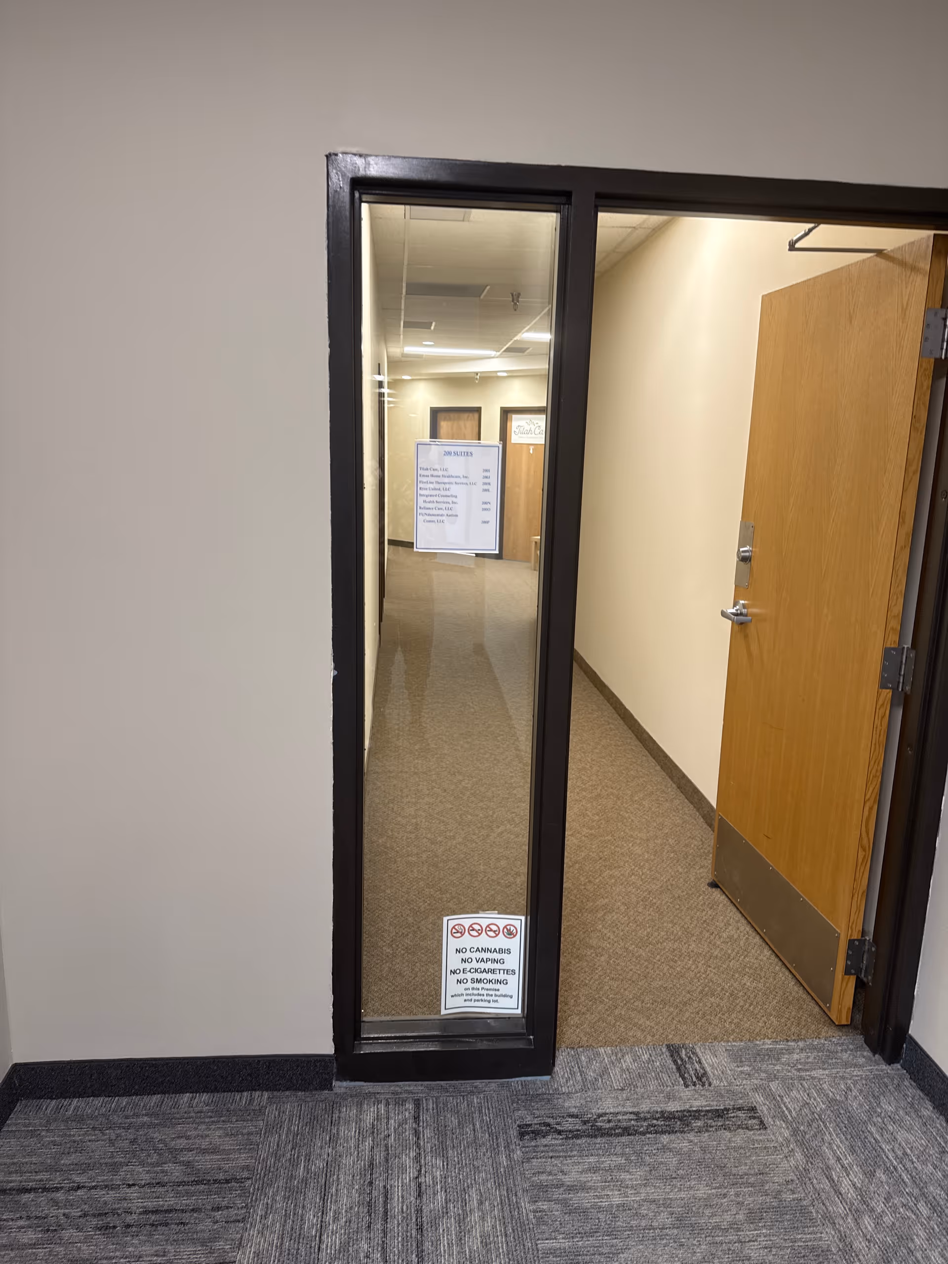 Interior hallway with a glass-framed doorway and signs along beige walls.