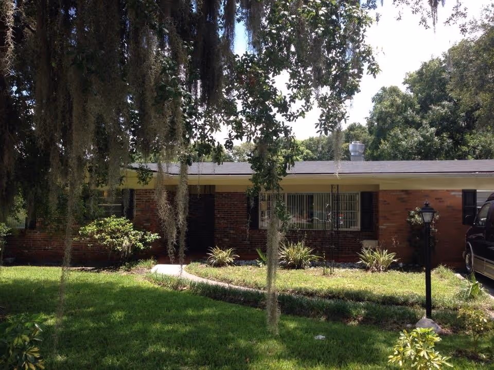 Brick single-story building with lawn, shrubs, and hanging moss in front.