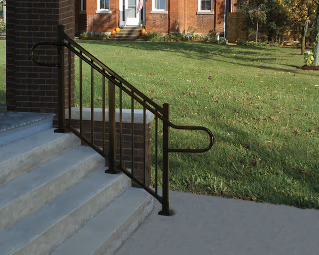 Brick building entrance with concrete steps and black metal handrail beside a grassy lawn.
