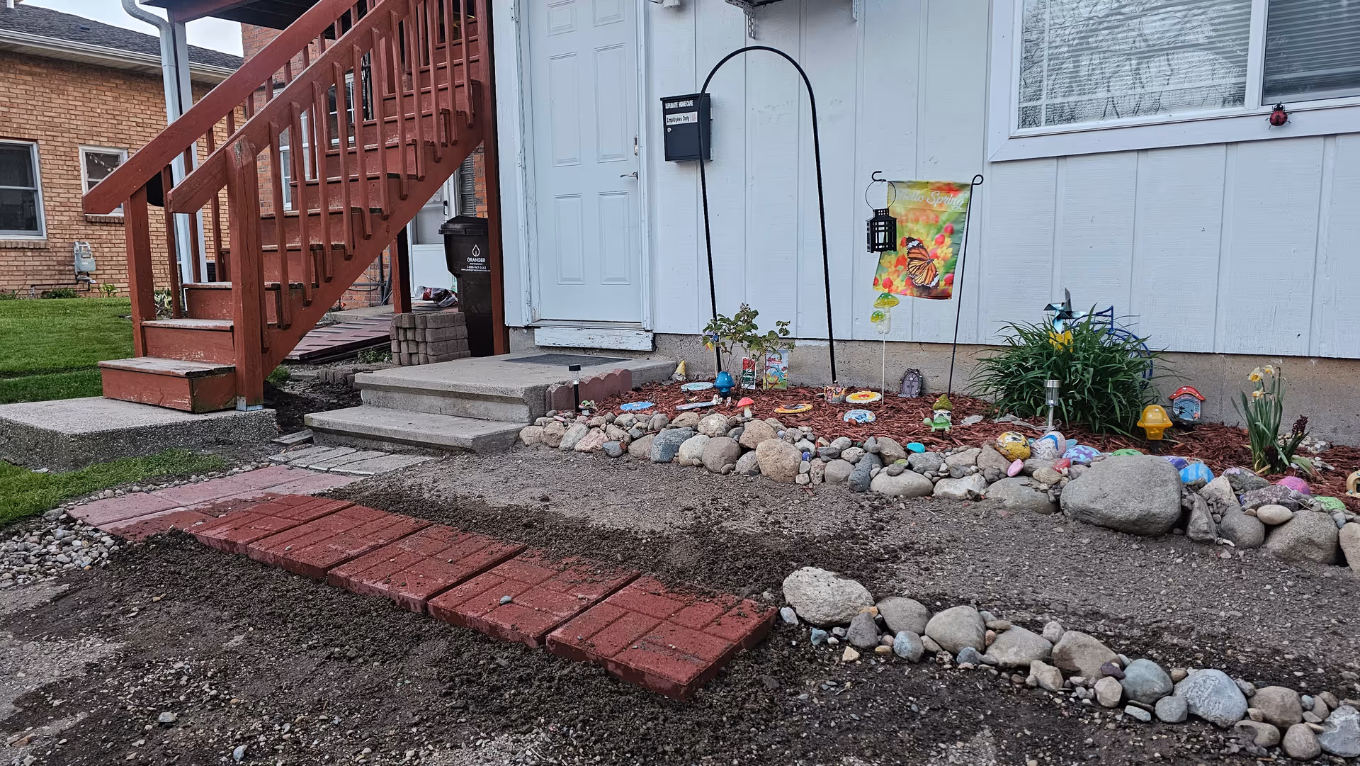 Front entrance of a light-blue house with red stairs and a rock-edged garden.